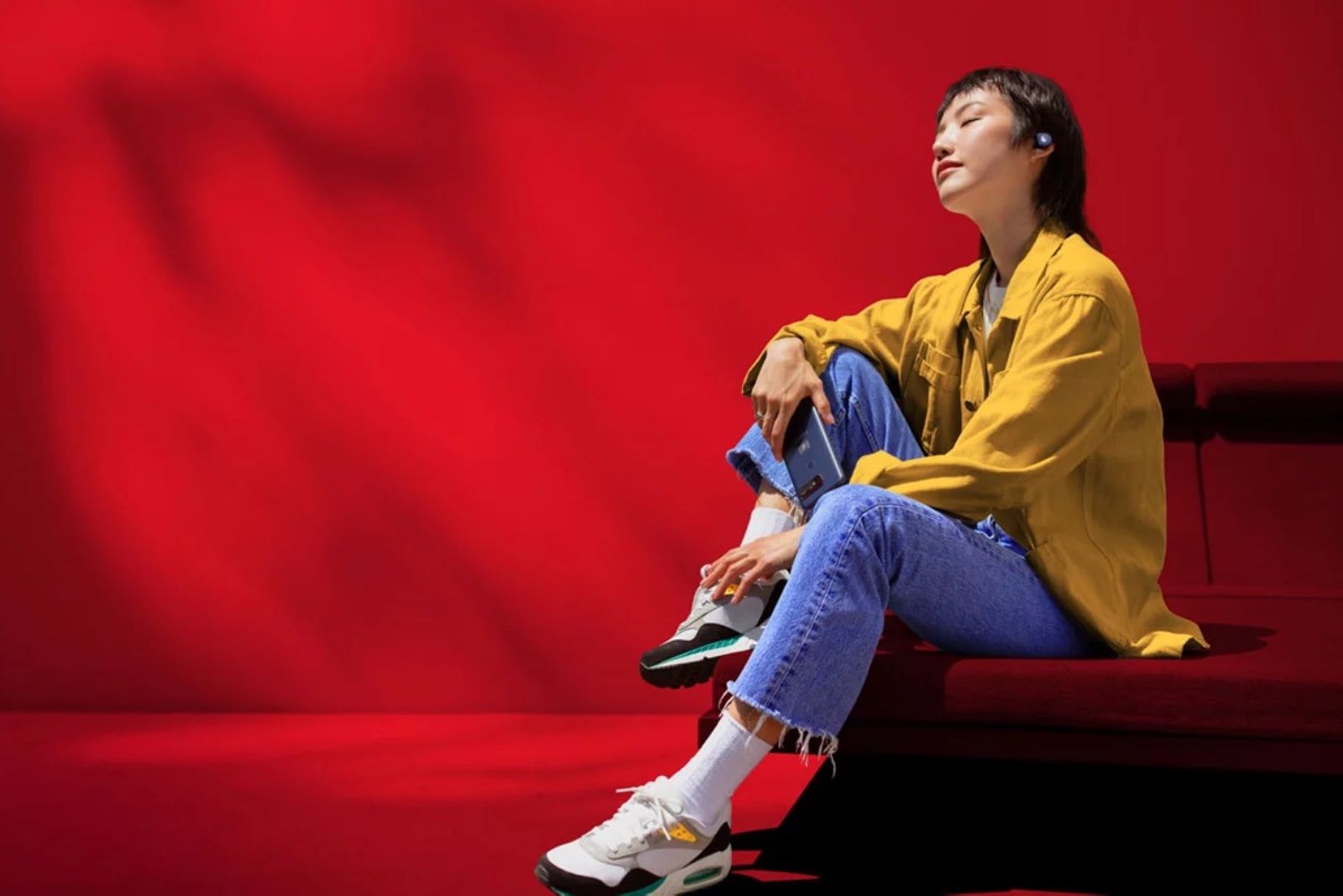 Person in yellow jacket, blue jeans wearing earbuds.