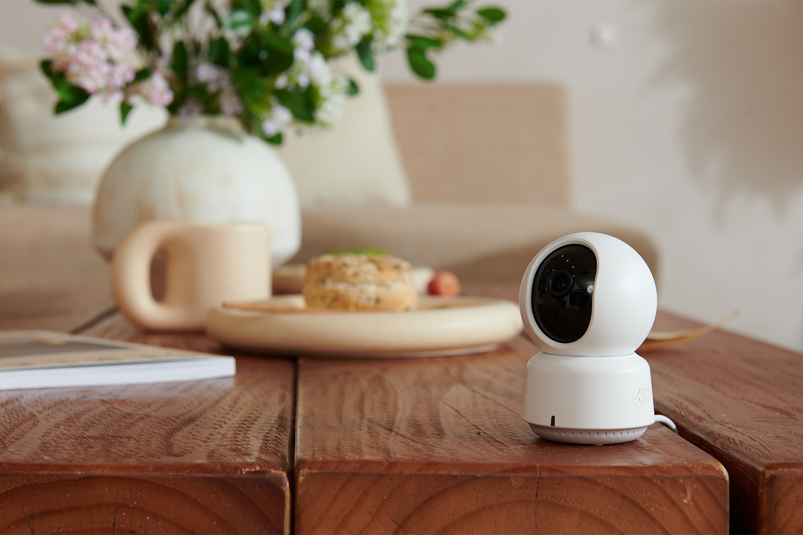 A white security camera sits on a wooden table