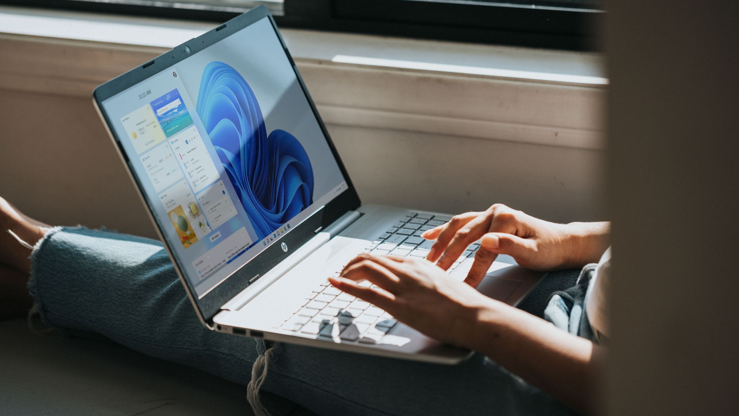 Feature image person sitting in front of window on ground legs outstretched with laptop running Windows 11