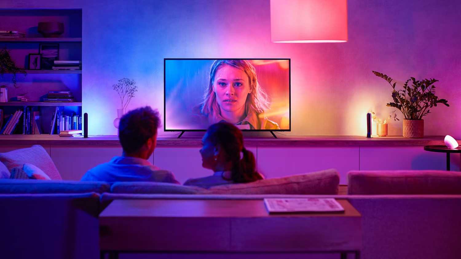 A couple watching TV in a dark room with ambient smart lighting.