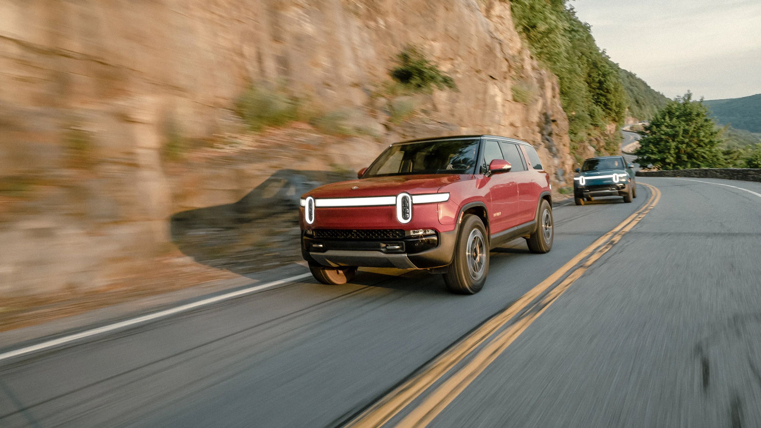 A Rivian R1S and R1T drive along a mountain road