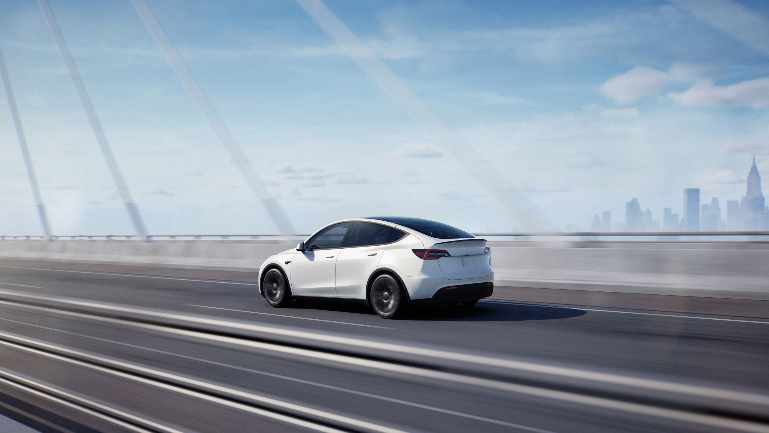 A white Tesla Model Y travels across a suspension bridge