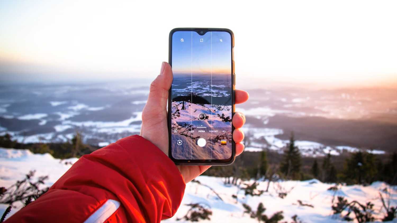A person takes a photo of a snowy sunset with their phone