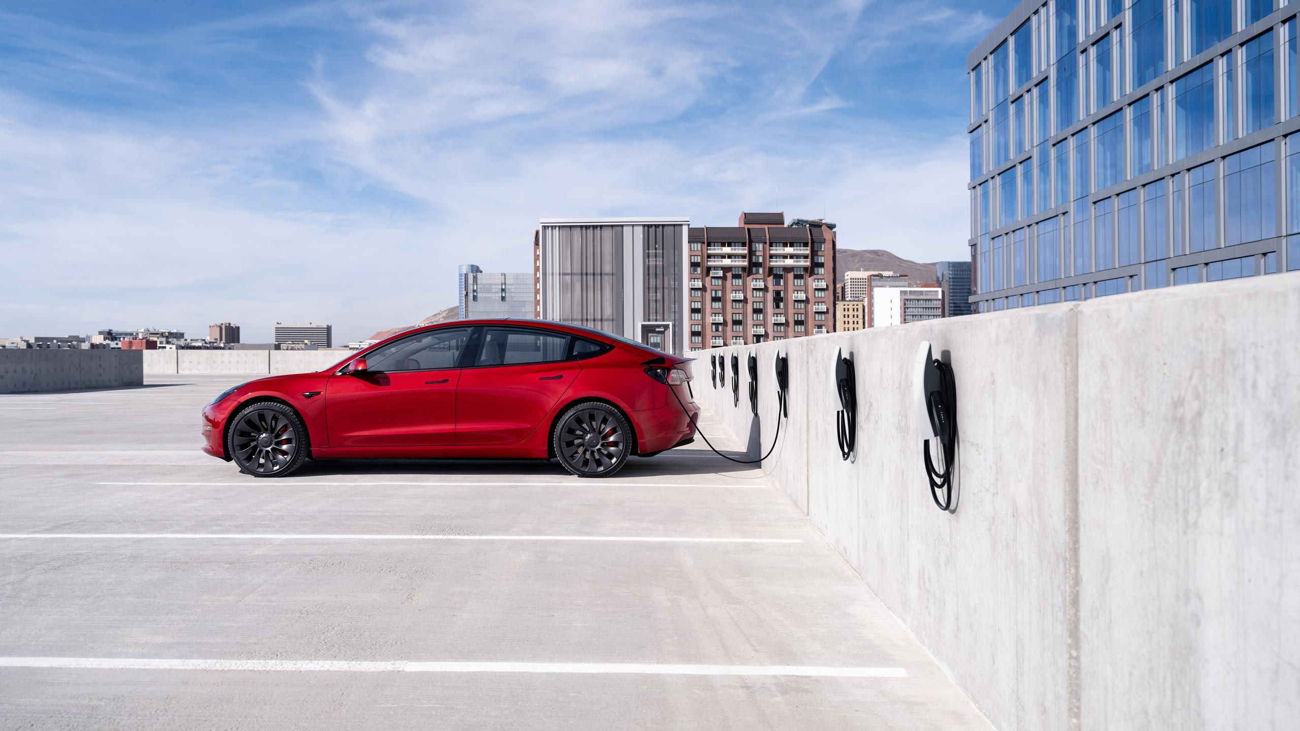 A red Tesla Model 3 charges on a rooftop parking garage