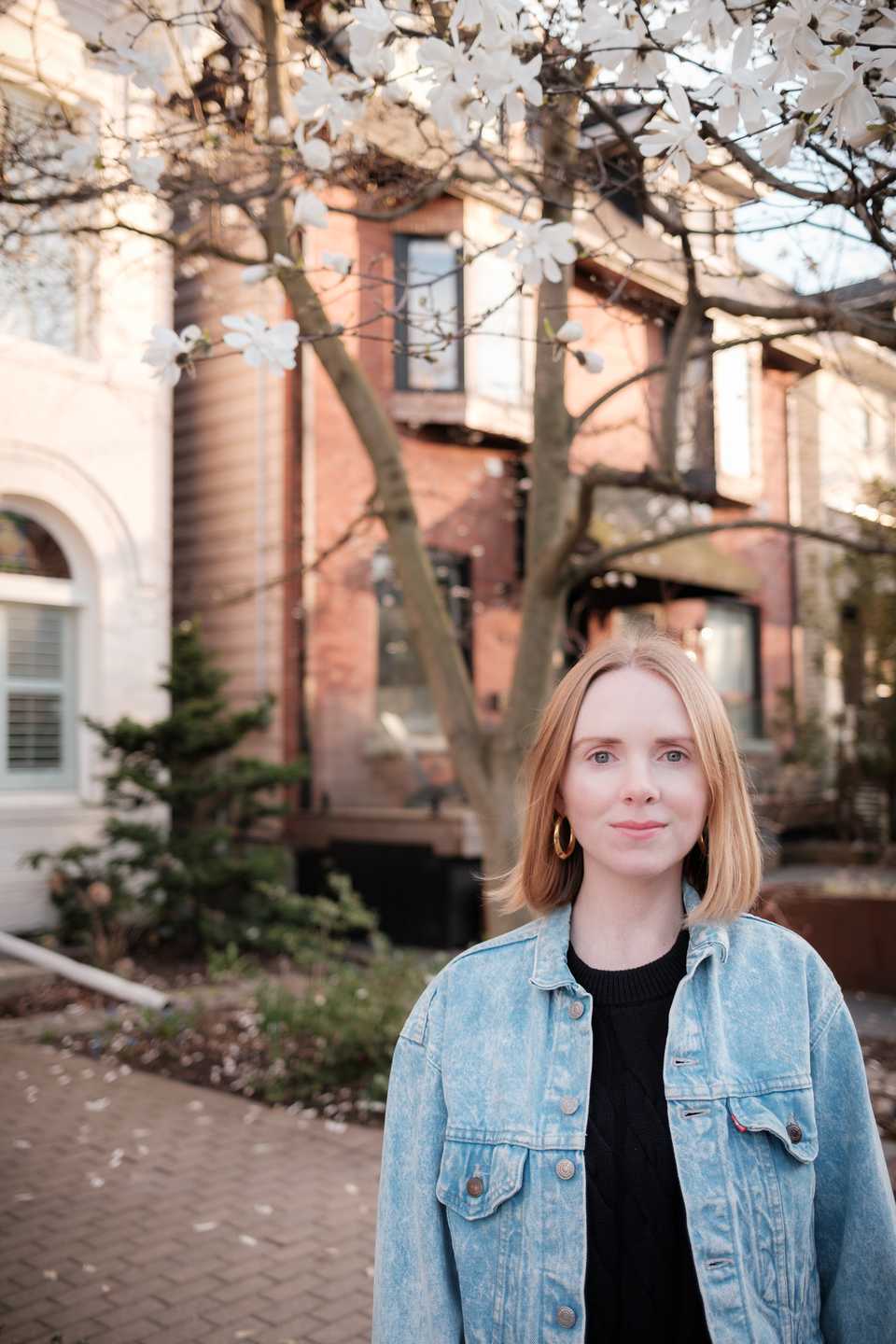 A blonde, fair skinned woman stands in front of a cherry blossom tree