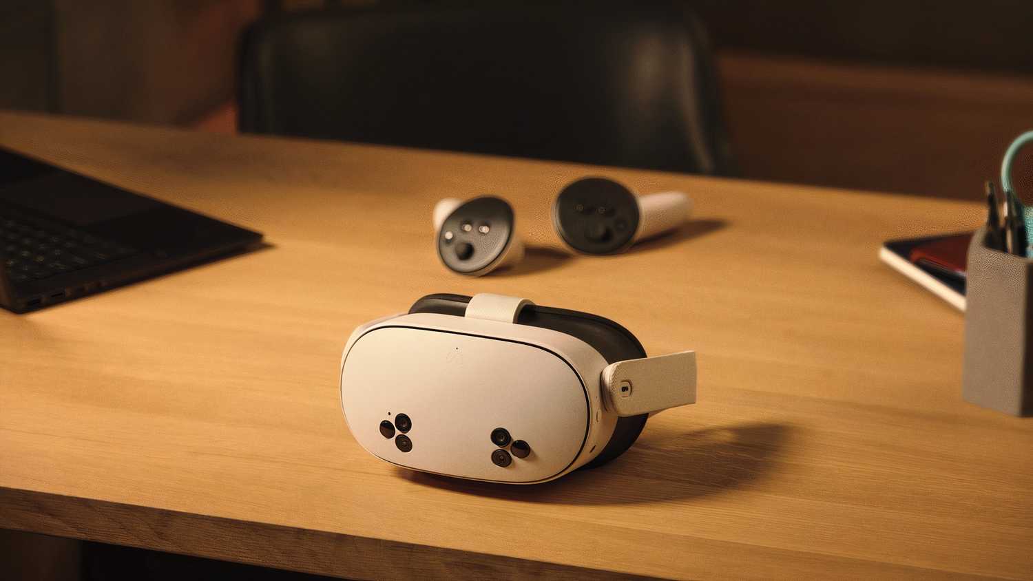 A white VR headset with six black cutouts on the front laying in front of some round VR controllers.