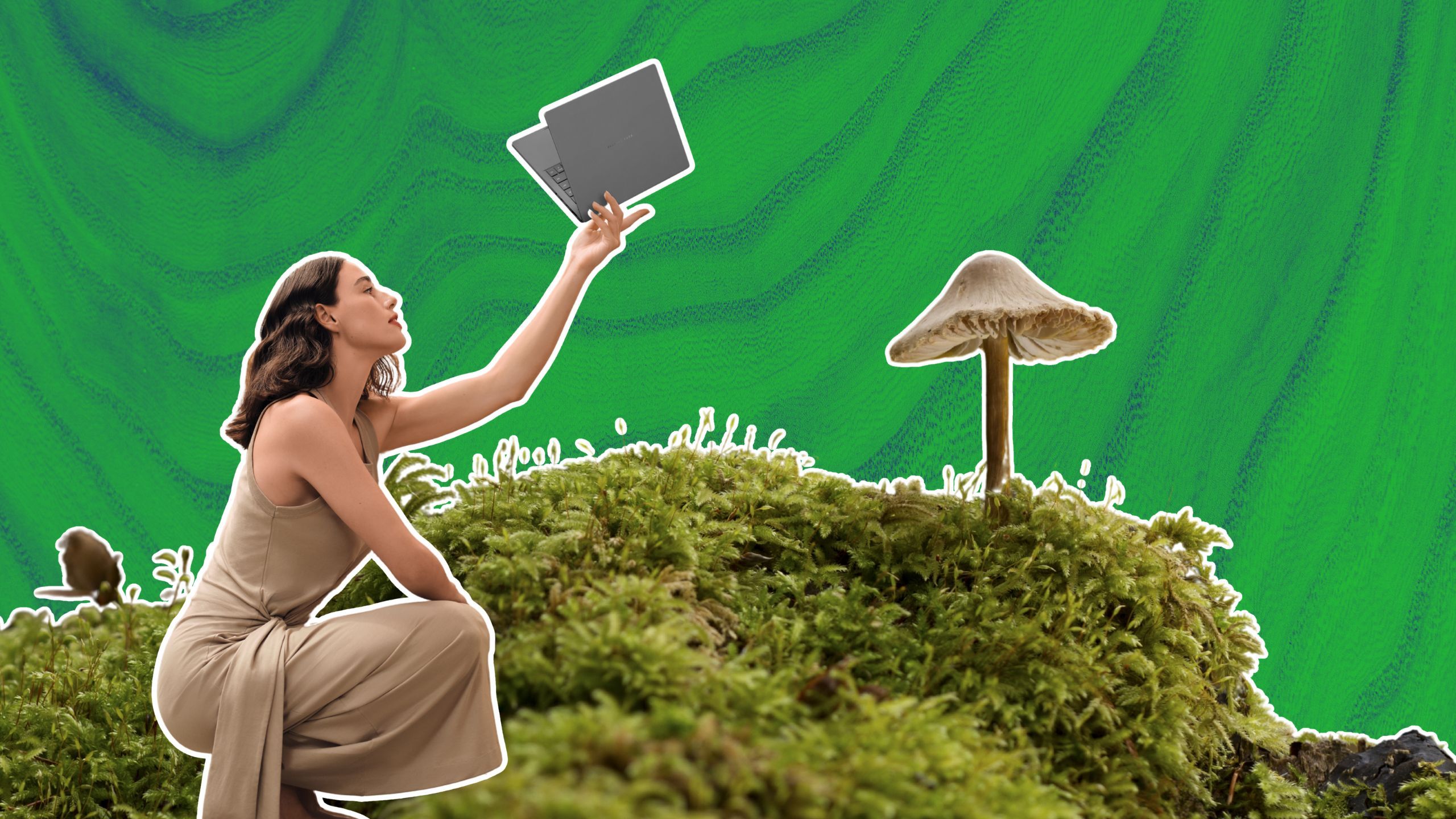 A woman holding a laptop beside moss and a mushroom. 