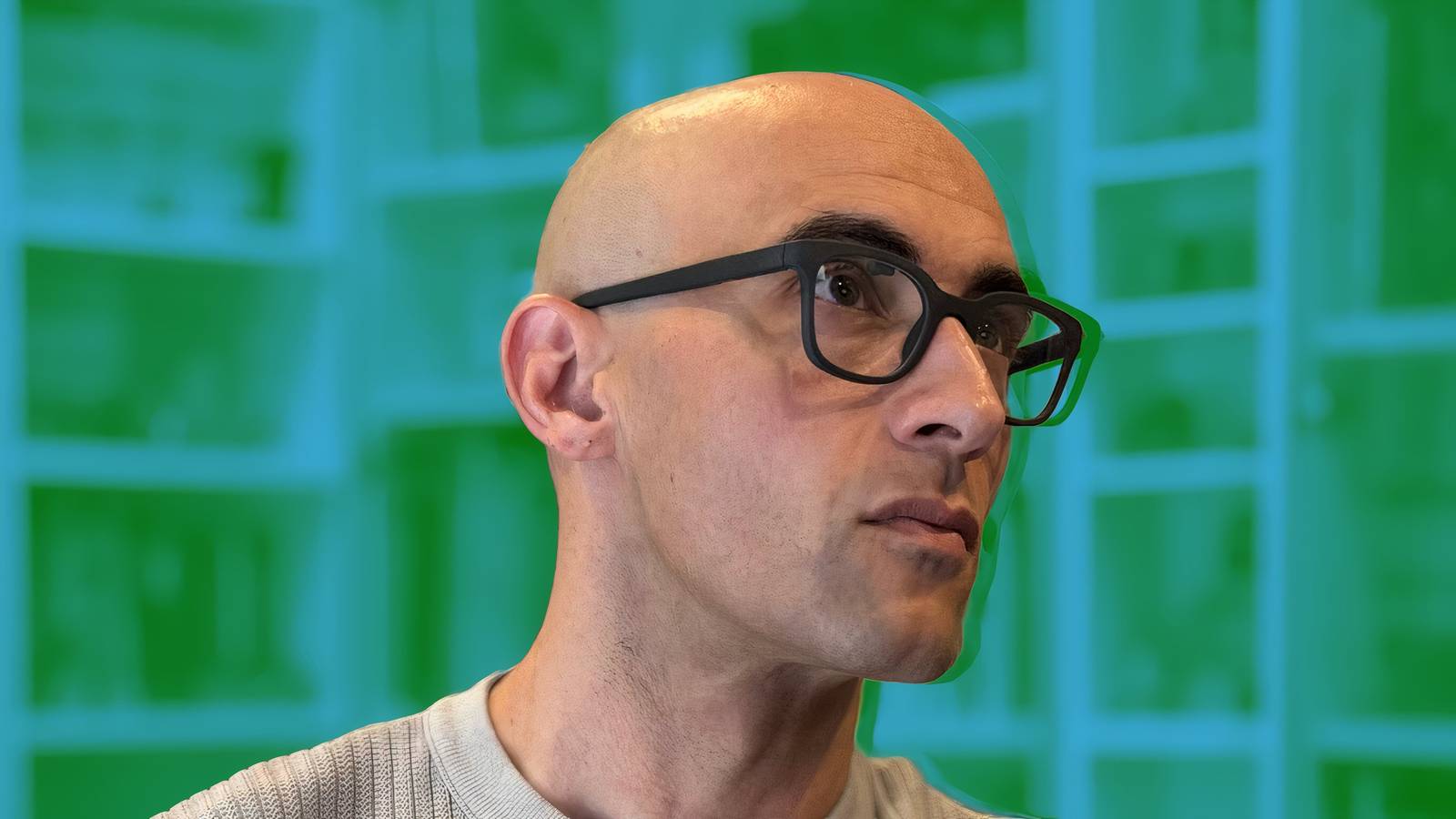 A person wearing black Halo smart glasses in front of a bookcase that's been edited to be blue and green.