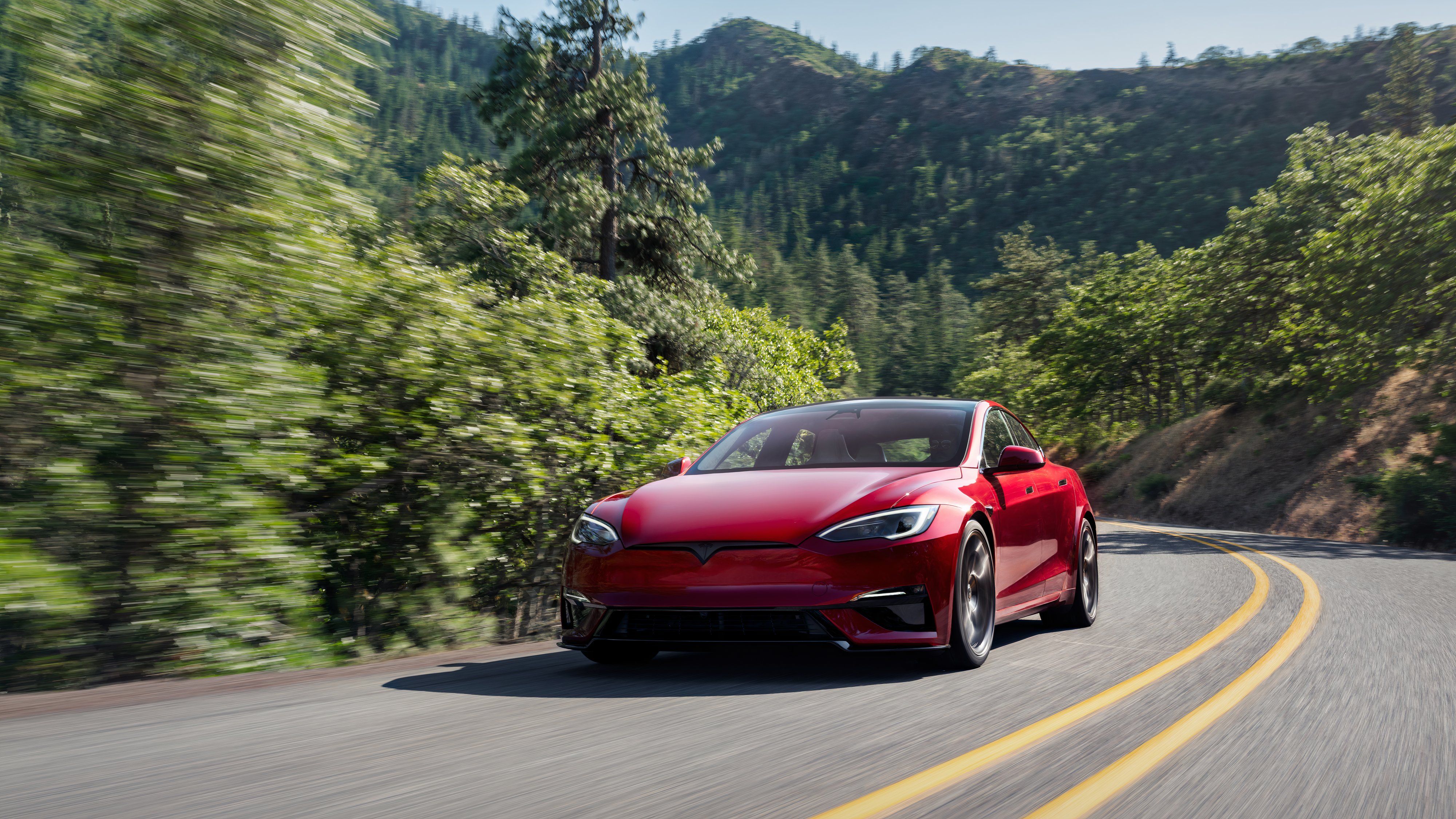 A still photo of a Tesla Model S driving on a two-lane road. 