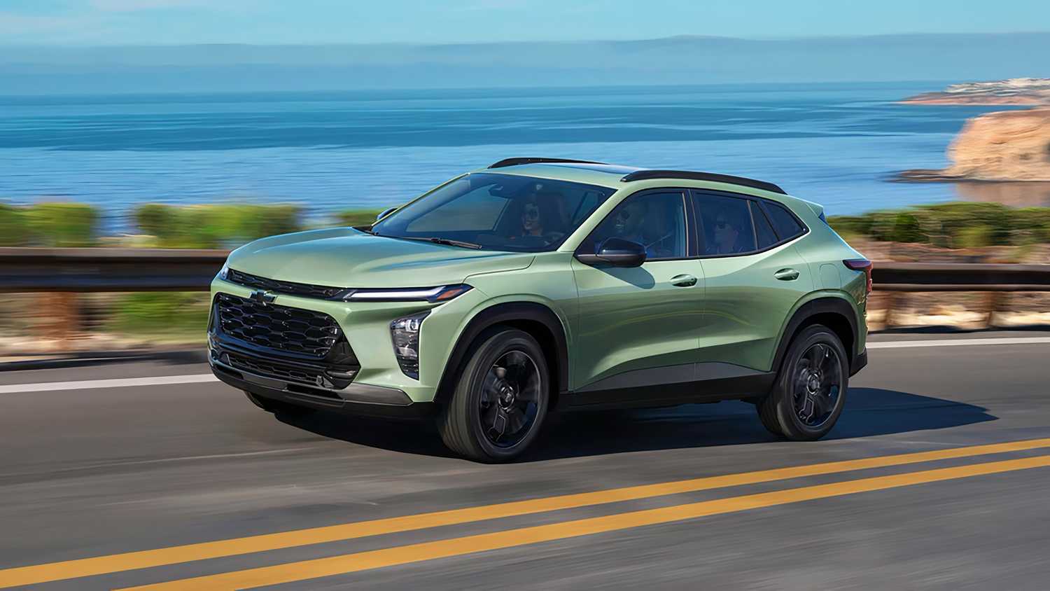A green Chevy driving alongside the water. 
