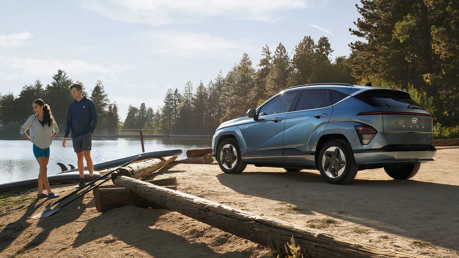 A still photo of a Hyundai Kona Electric parked beside a lake and two people. 