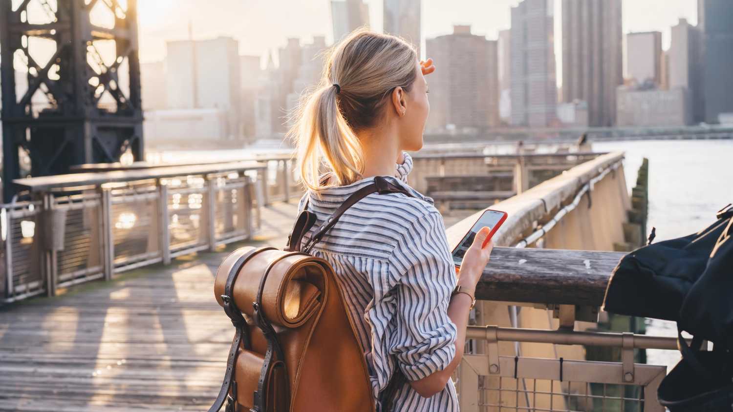woman looking across the water at the skyline with phone in hand - yesim