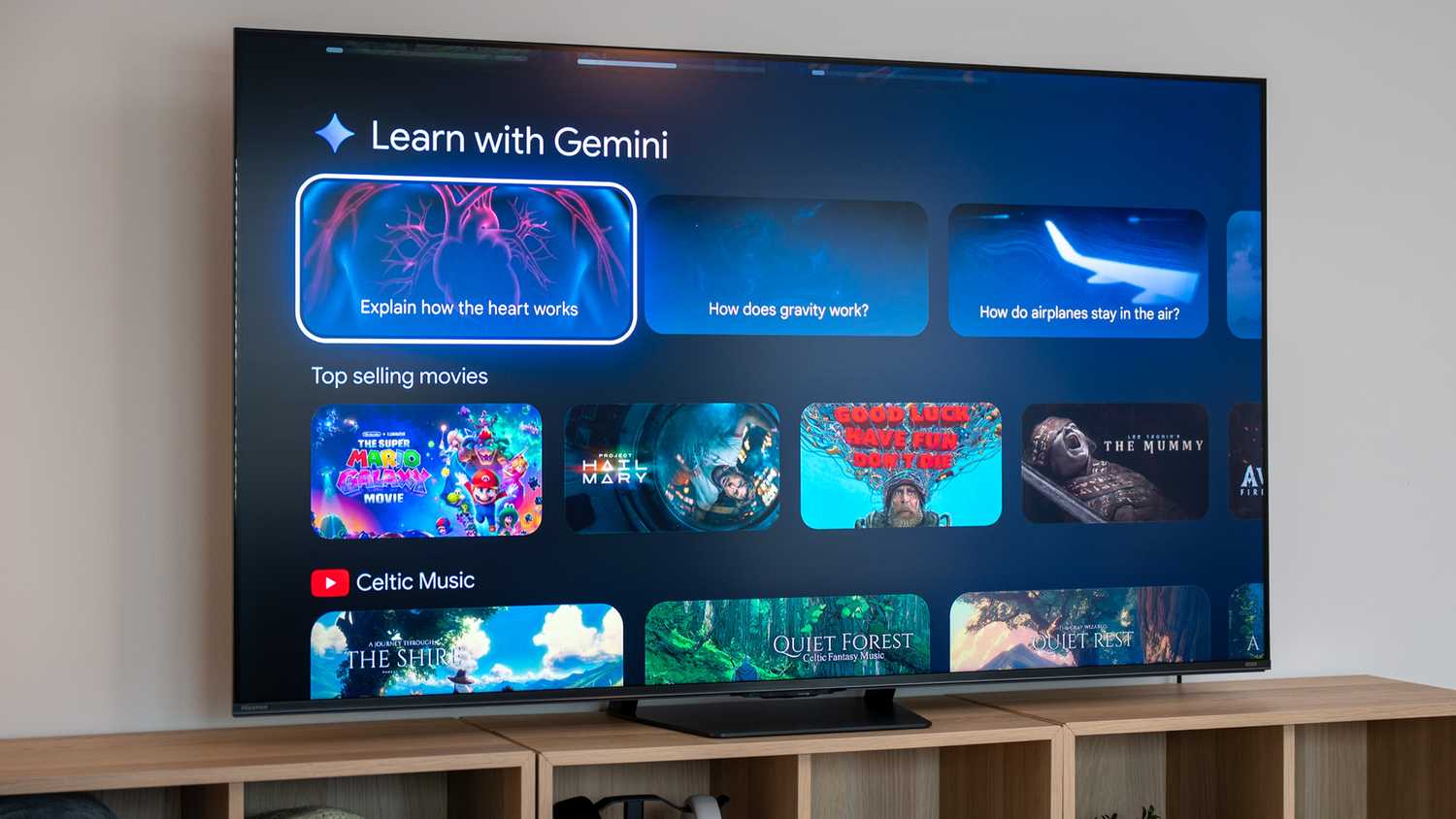 The Hisense U7 on a wooden media console displaying the Google TV home screen with Learn with Gemini and movie recommendations.