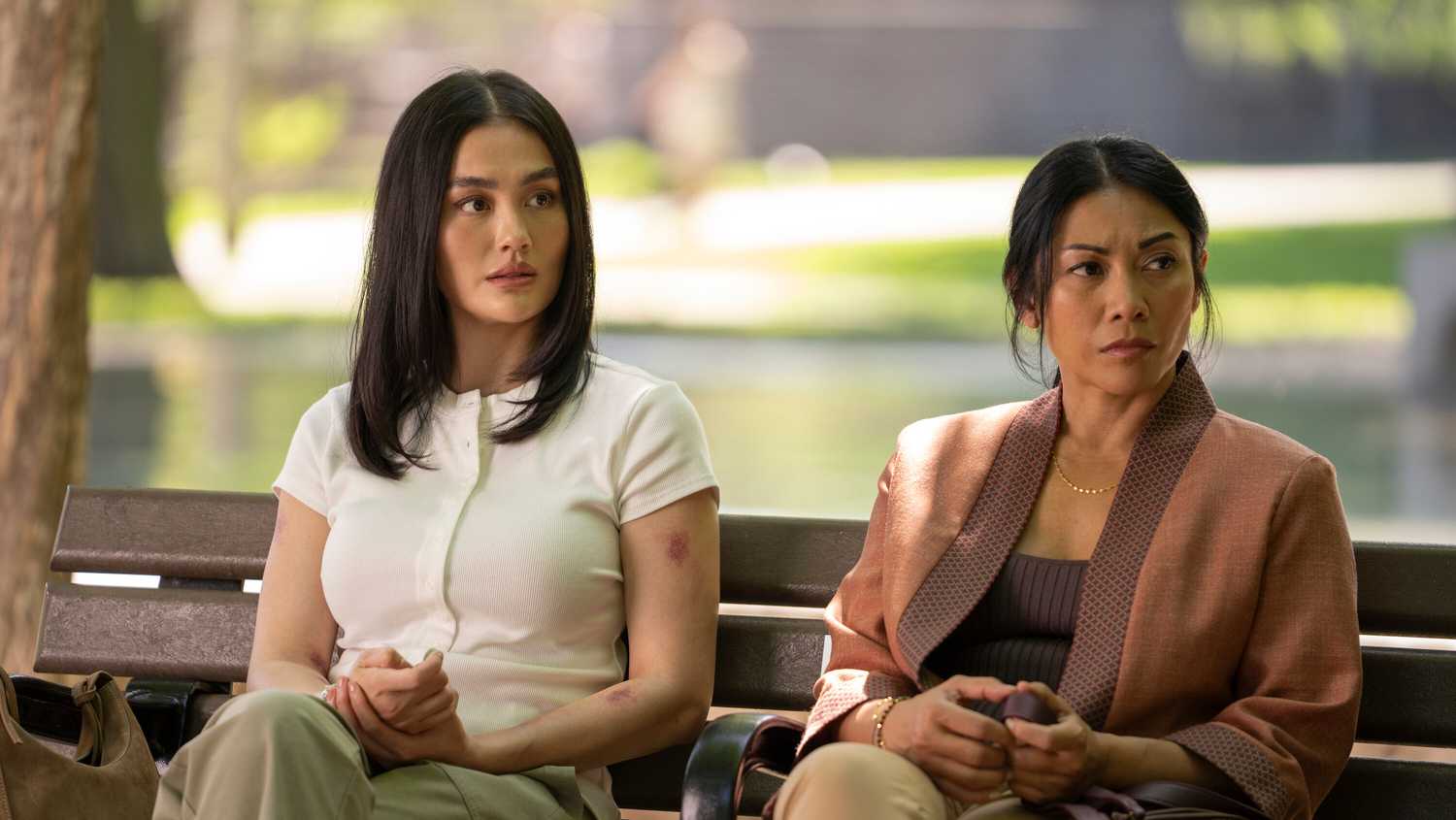 Agnez Mo and Anggun sitting together outside on a park bench in Reacher season 4.