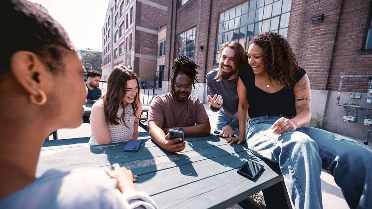 Group of people sitting at a table looking at a phone.