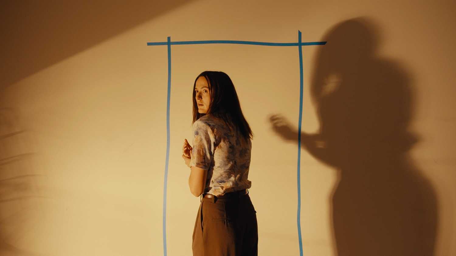 Renate Reinsve standing in front of a doorway taped to a wall in Backrooms