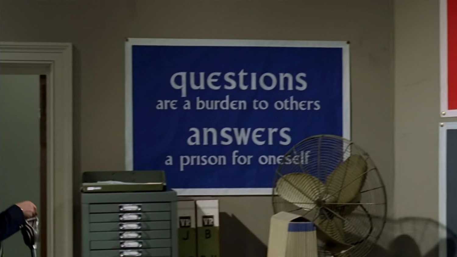 A sign from The Prisoner that says "Questions are a burden to others, Answers a prison for oneself."