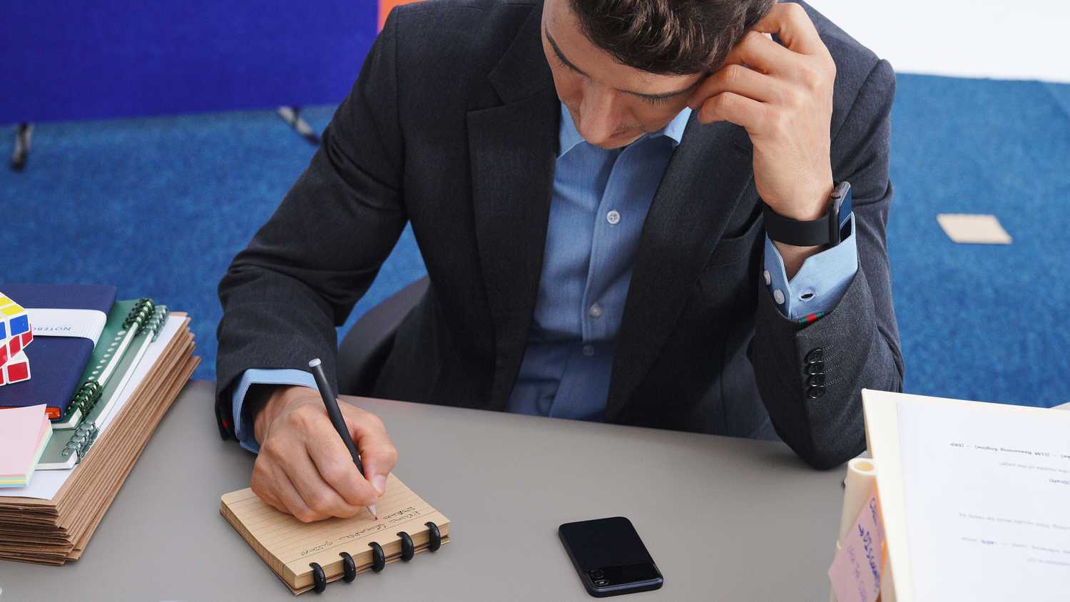 Man writing in a notepad with the Comu Action Pro sitting on the desk beside him.