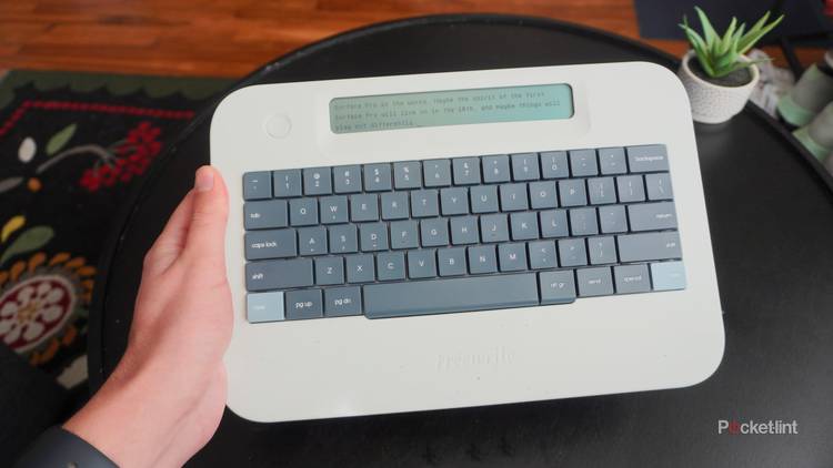 A hand holding the Freewrite alpha over a black coffee table.