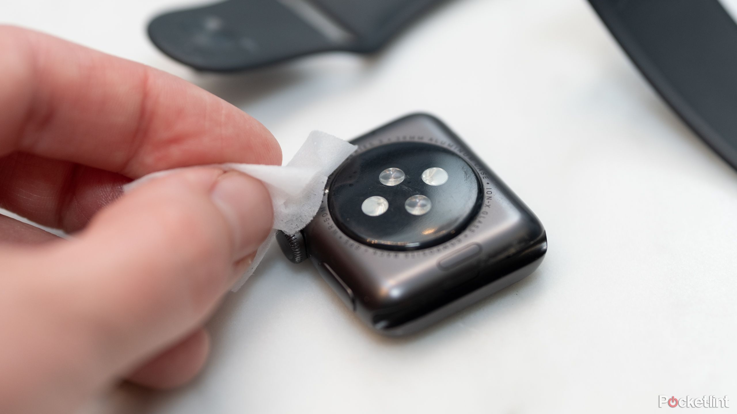 A hand cleans a smartwatch with an alcohol wipe.