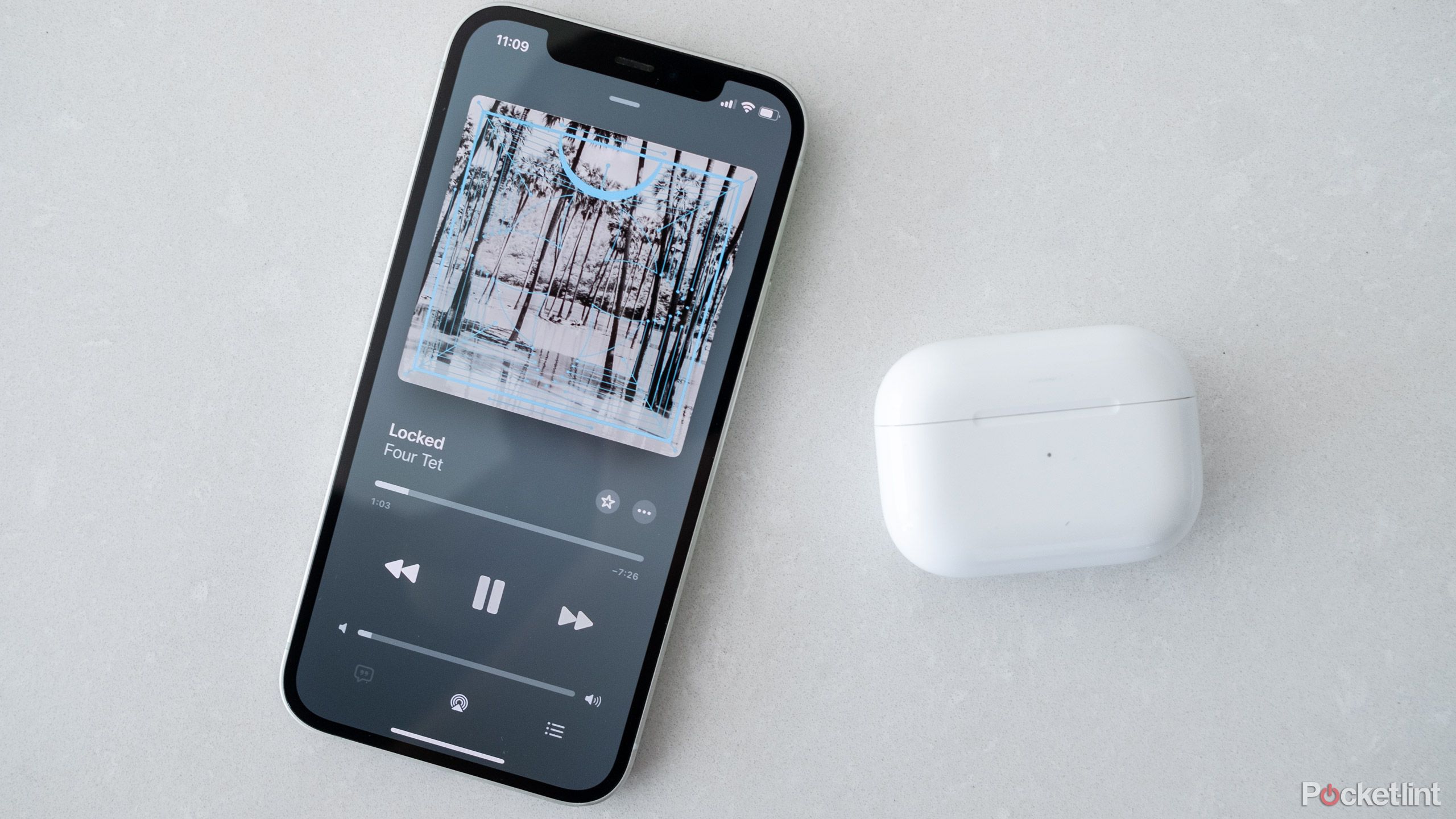 An iPhone 12 with Apple Music on the screen and an AirPods Pro case next to it