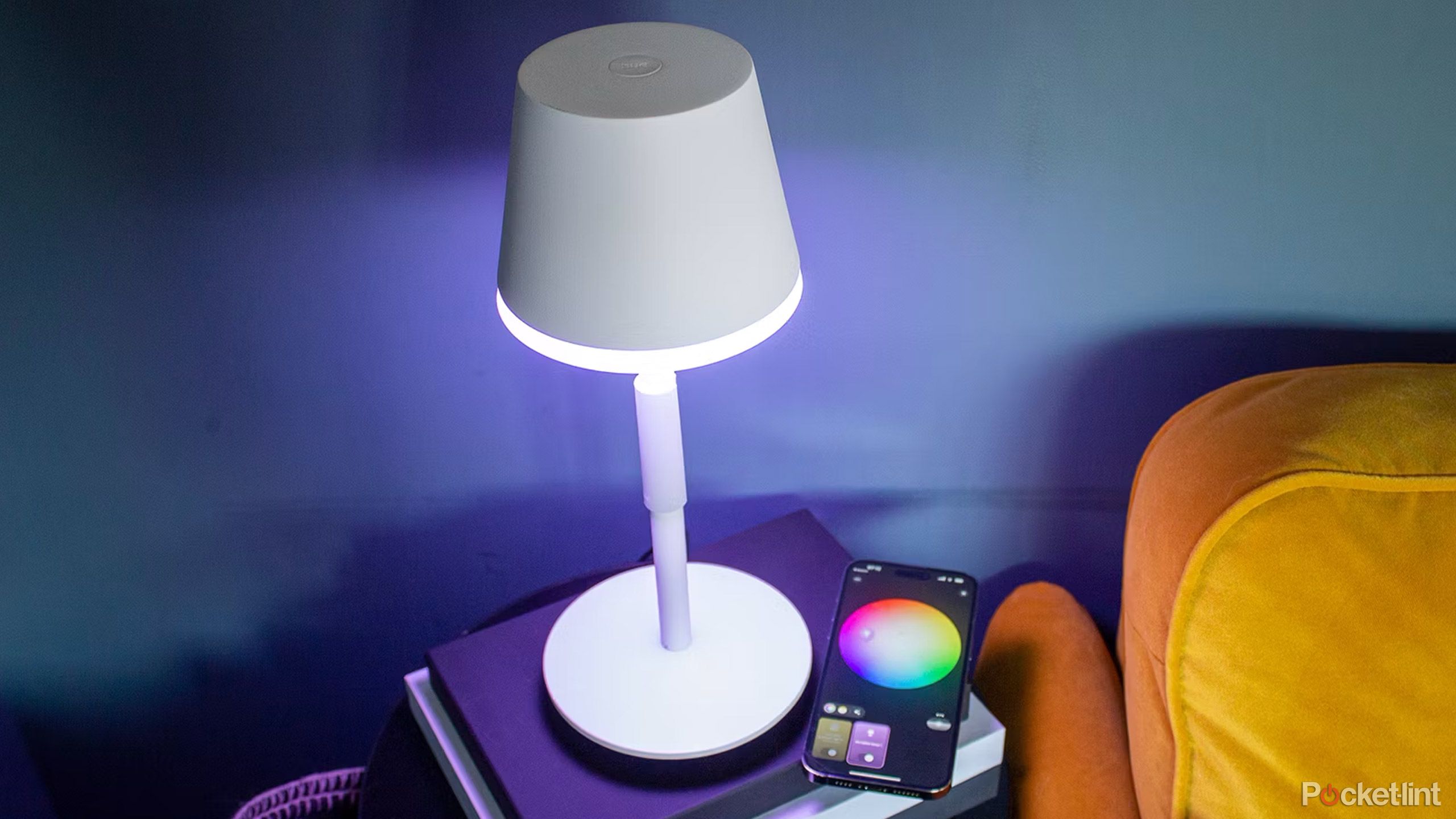 An iPhone with the Philips Hue app sits on a beside table next to a lamp.