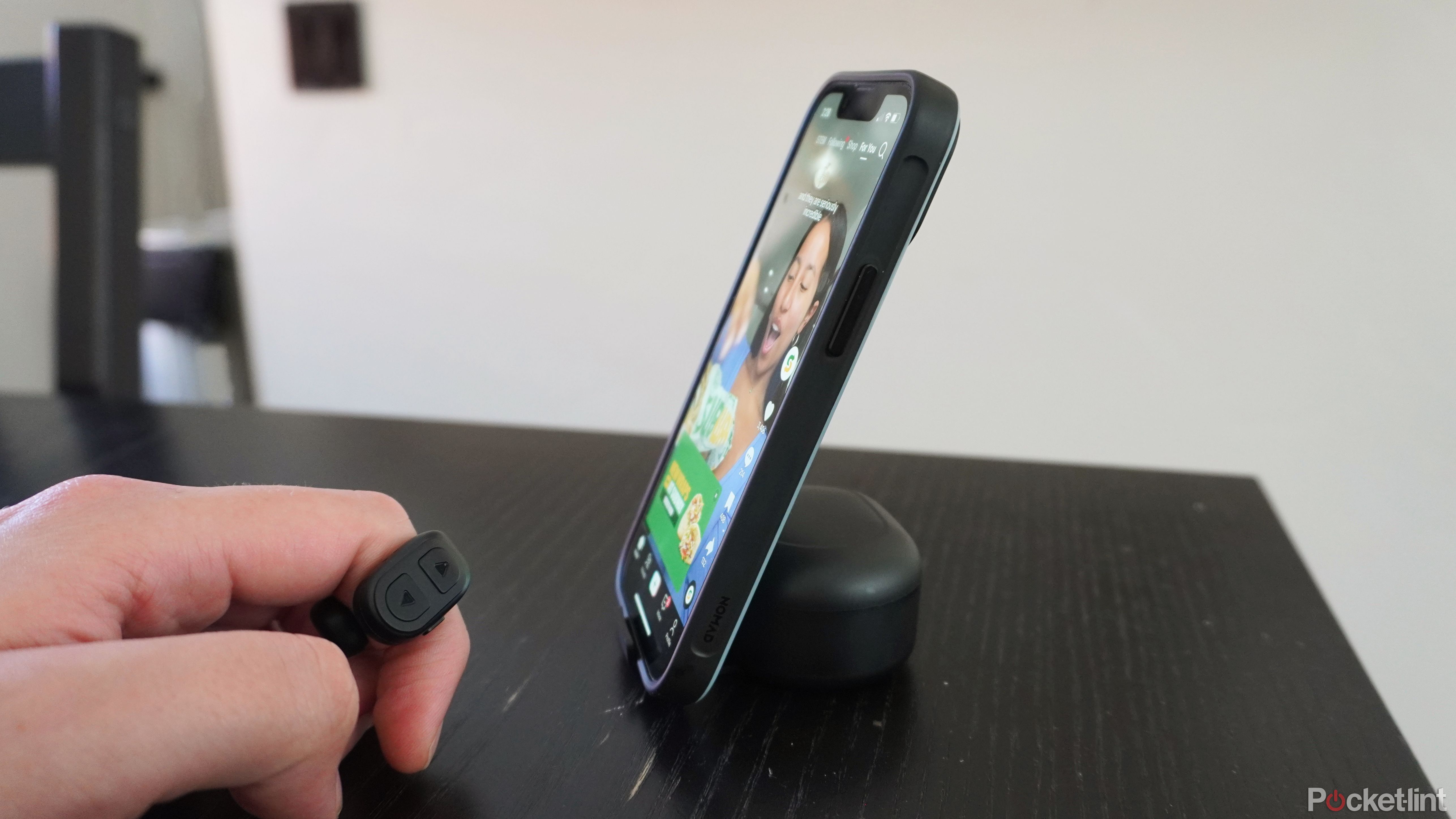 An iPhone perched on a charging case with a ring remote in view.
