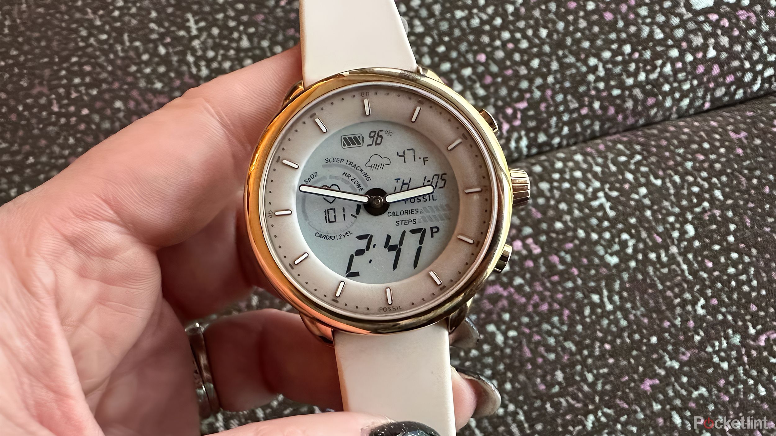 A hand holds a Fossil smartwatch.