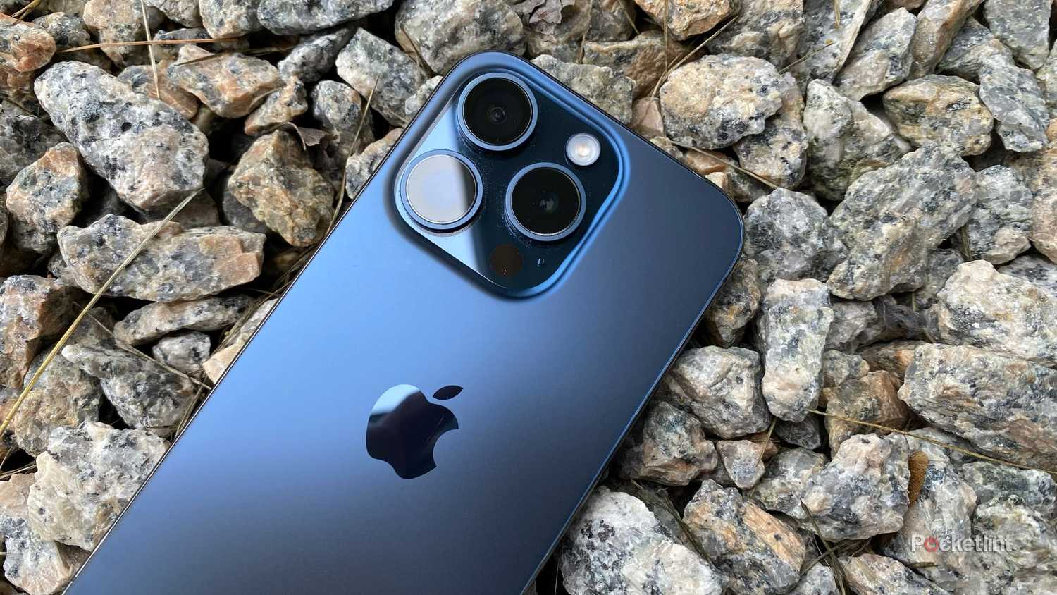 A blue iPhone 15 Pro on gravel.
