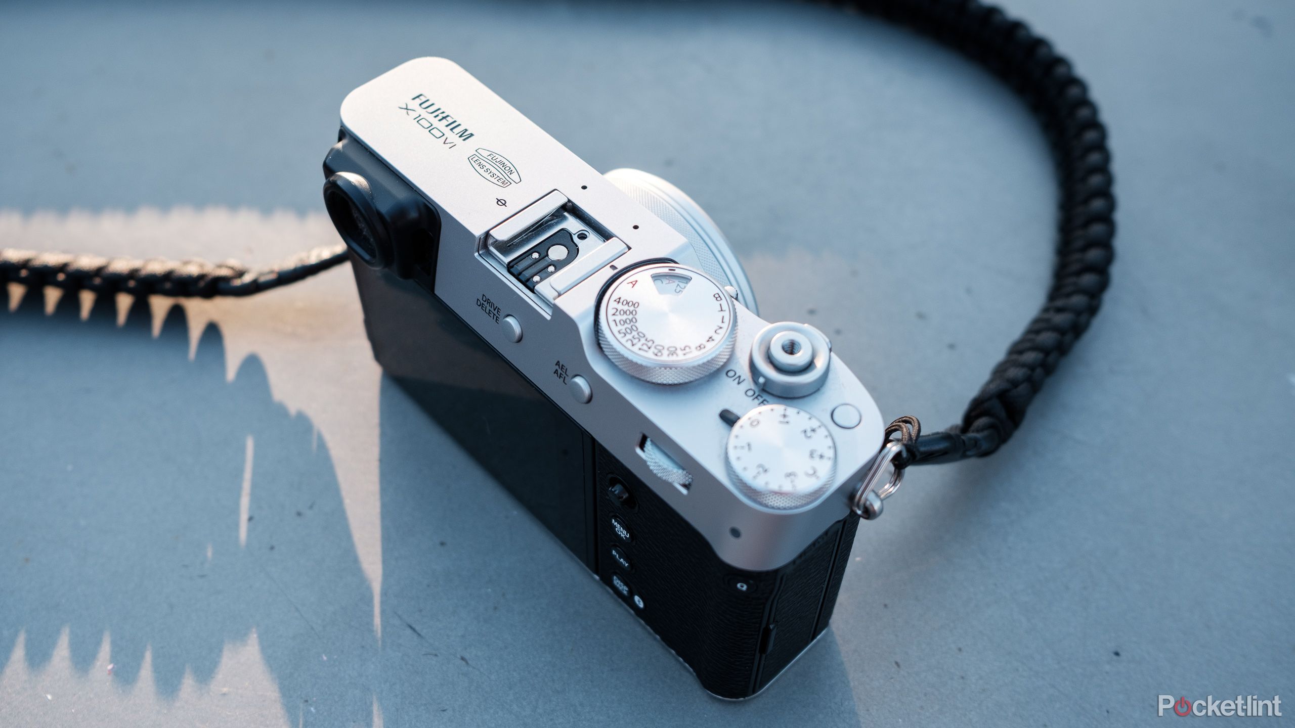 The X100VI sits on concrete, a golden hour sun illuminating part of the camera