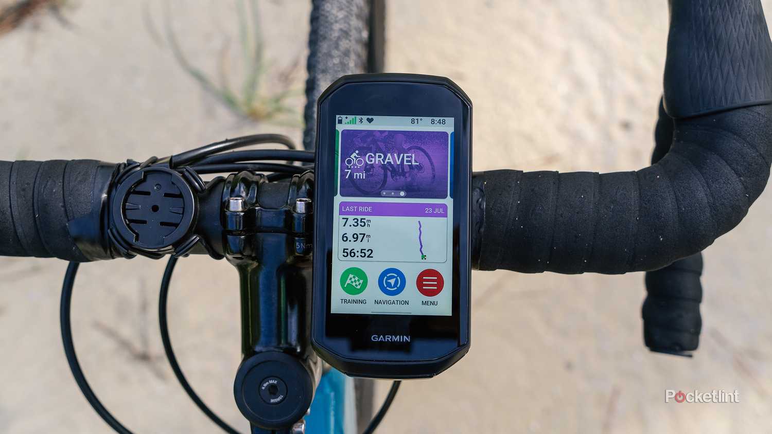 The Garmin Edge 1050 is mounted to bike handlebars with a blurred sandy road in the background.