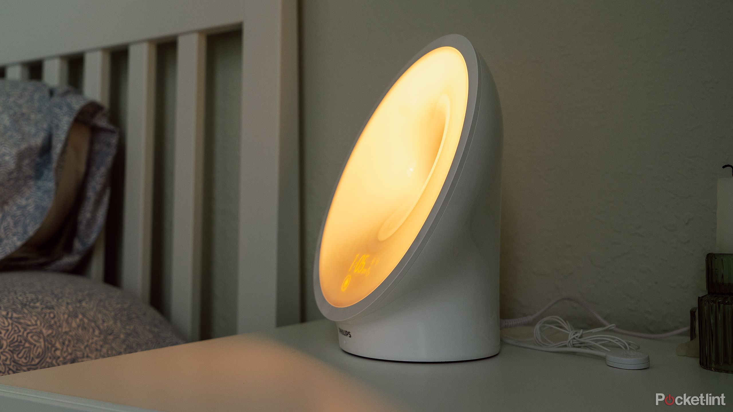 The Philips SmartSleep HF3670 glowing yellow on a white nightstand next to a bed. 