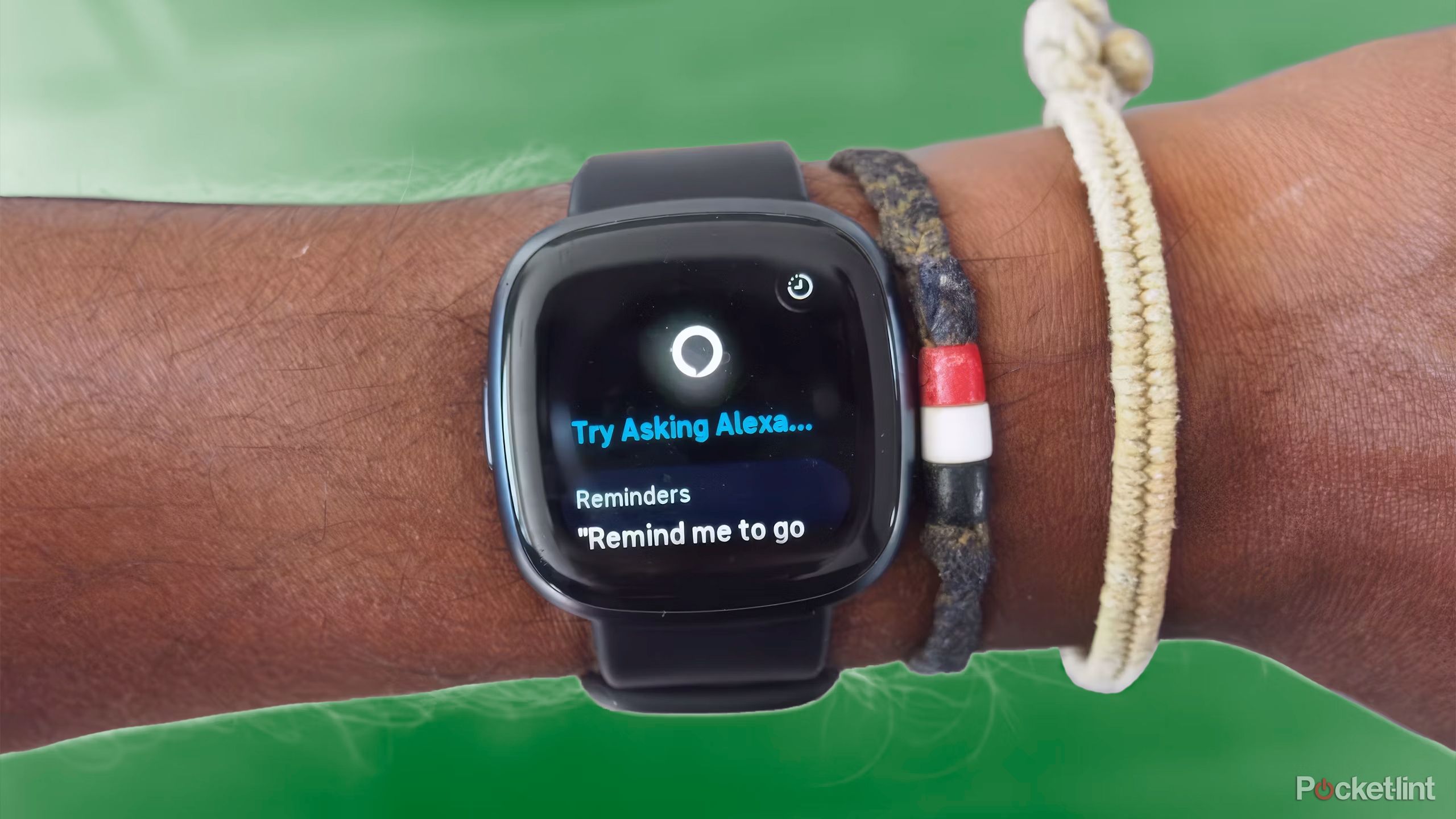 The Fitbit Versa 4 on a wrist with bracelets above a green background. 