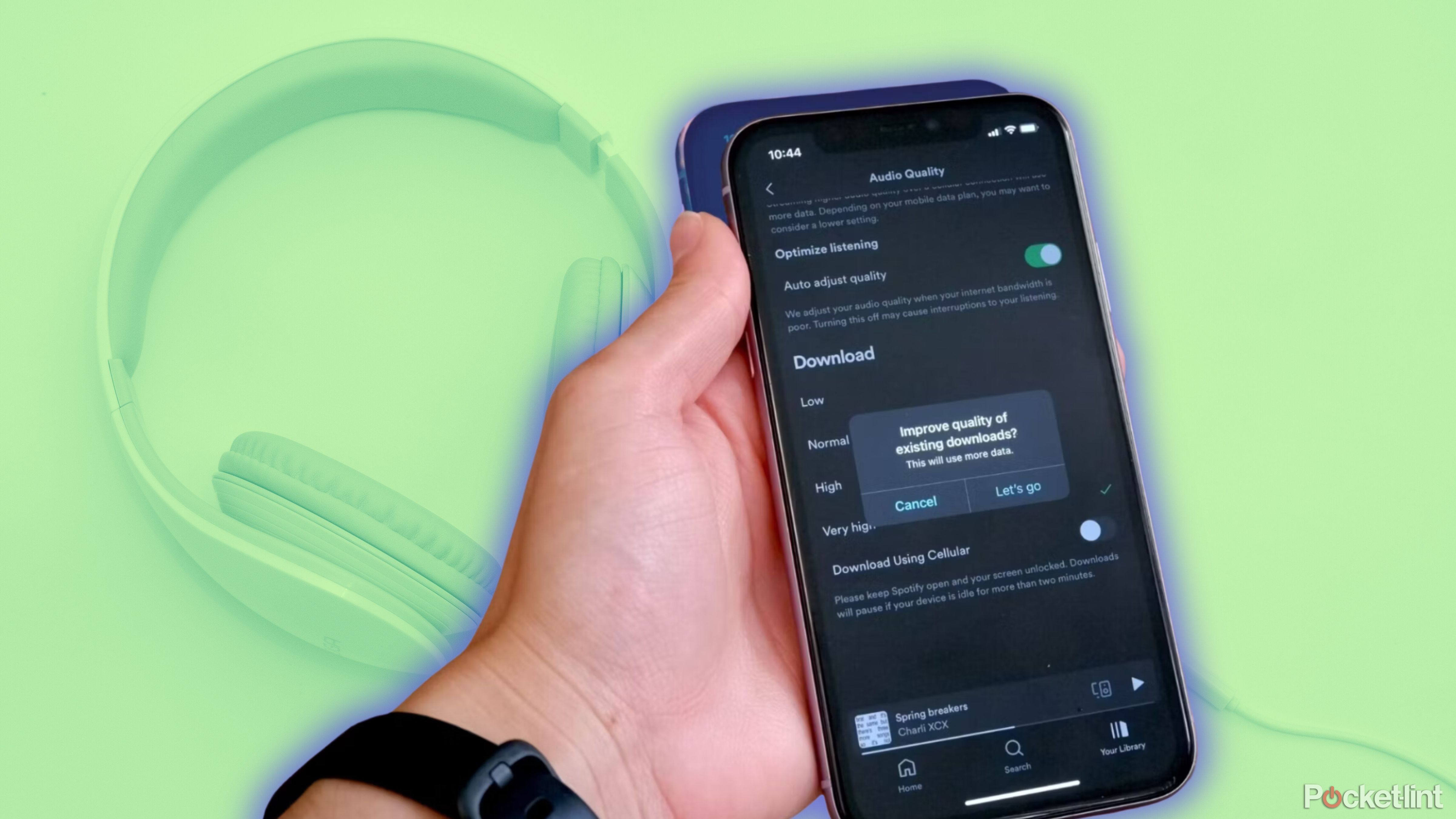 A hand holding an iPhone with Spotify open, showing the download quality settings page, with a pop up asking if you want to improve download quality