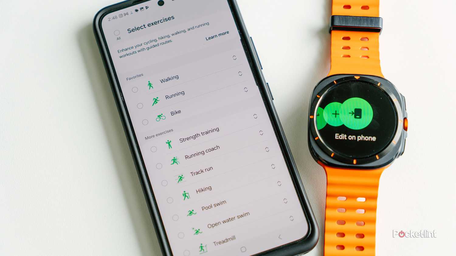 The Samsung Galaxy Watch Ultra rests on a white desk next to a Galaxy phone with the activity feature on the display. 