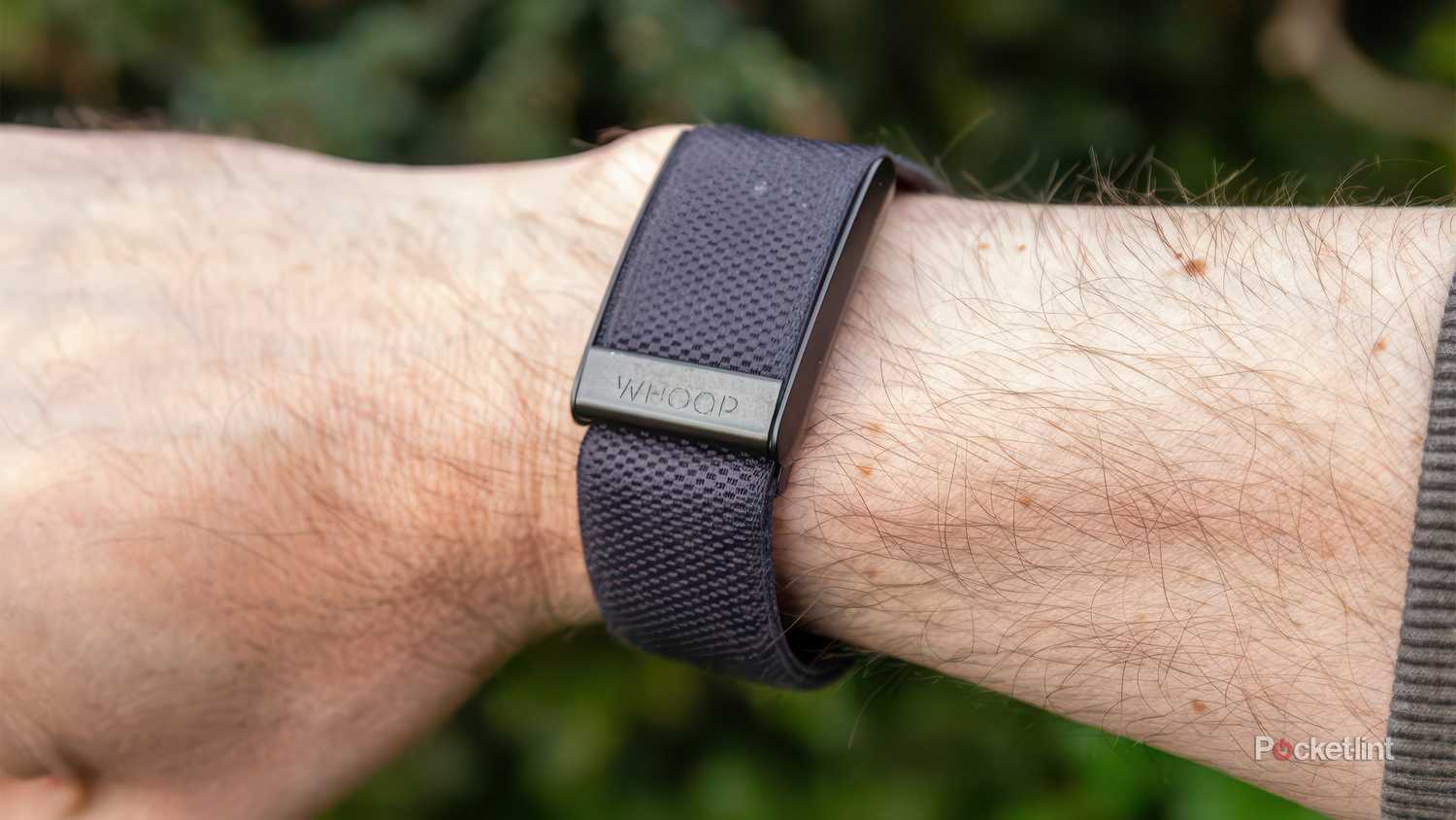 An Arm with the Whoop 4.0 is held in front of a blurred green background. 