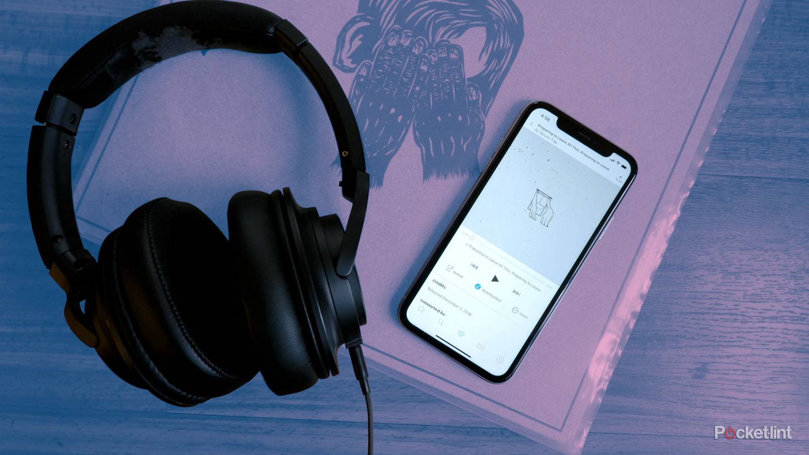 A pair of Audio-Technica headphones beside a phone streaming a song from Bandcamp, on top of a record