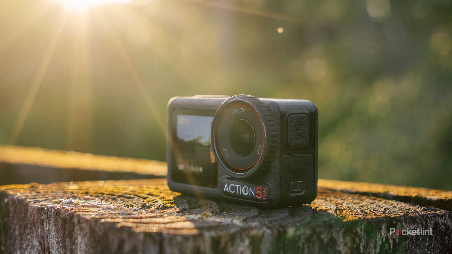The DJI Osmo Action 5 Pro sits on a weathered fence post with sun rays shining down on it. 
