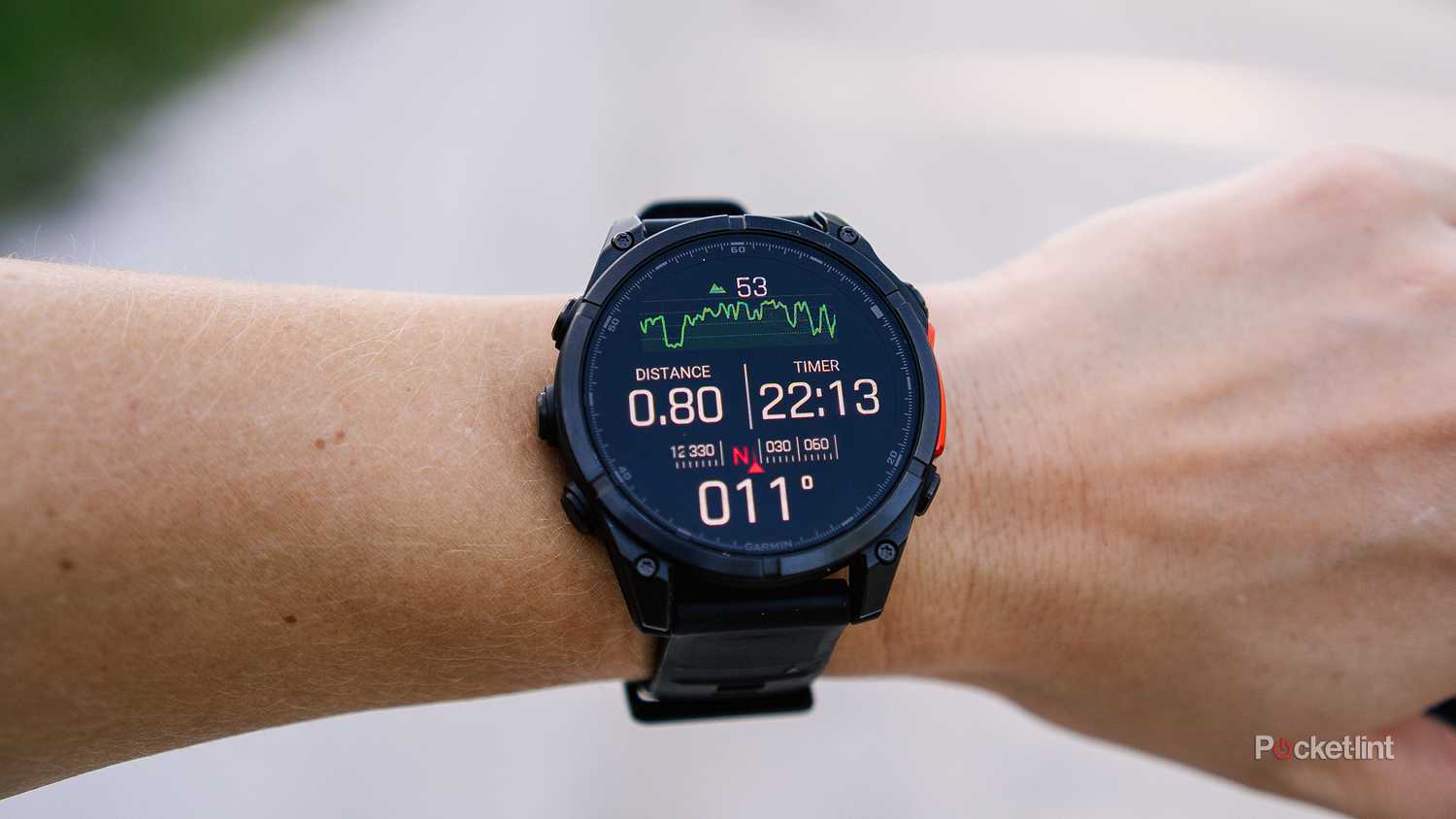 The Garmin Fenix 8 is on a wrist held in front of a blurred gravel road. 