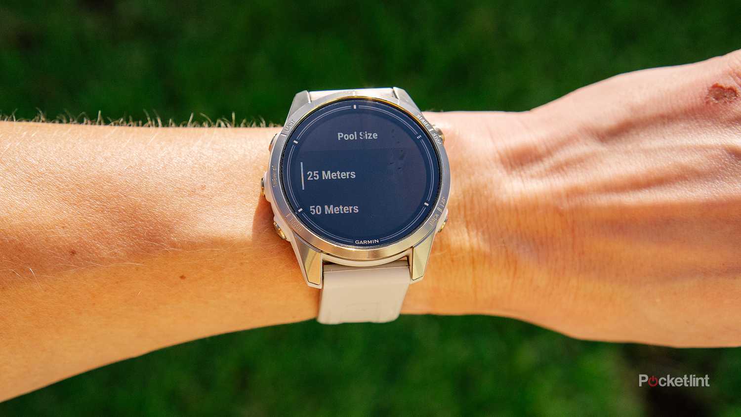 A wrist with the Garmin epix Pro Gen 2 Sapphire is held above blurred grass with the Pool Swim activity on the display. 