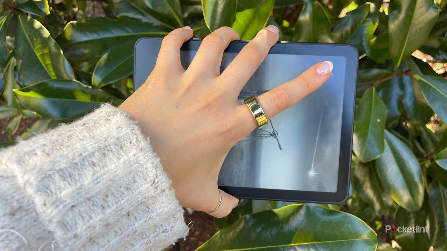 A woman holding a Kindle Paperwhite in front of foliage. 
