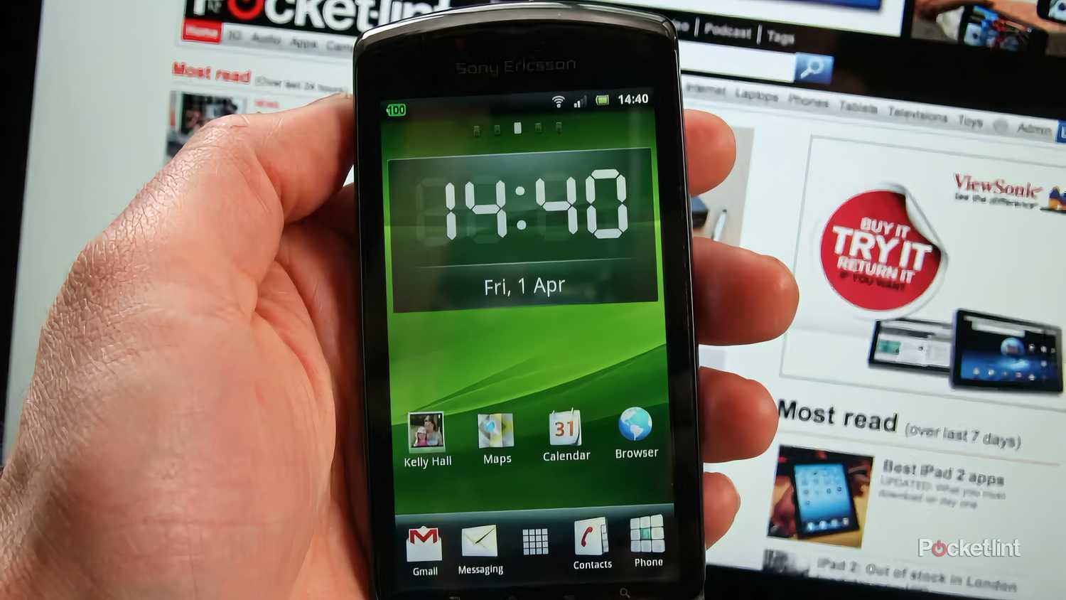 A hand holding a closed Xperia Play in front of a laptop screen.