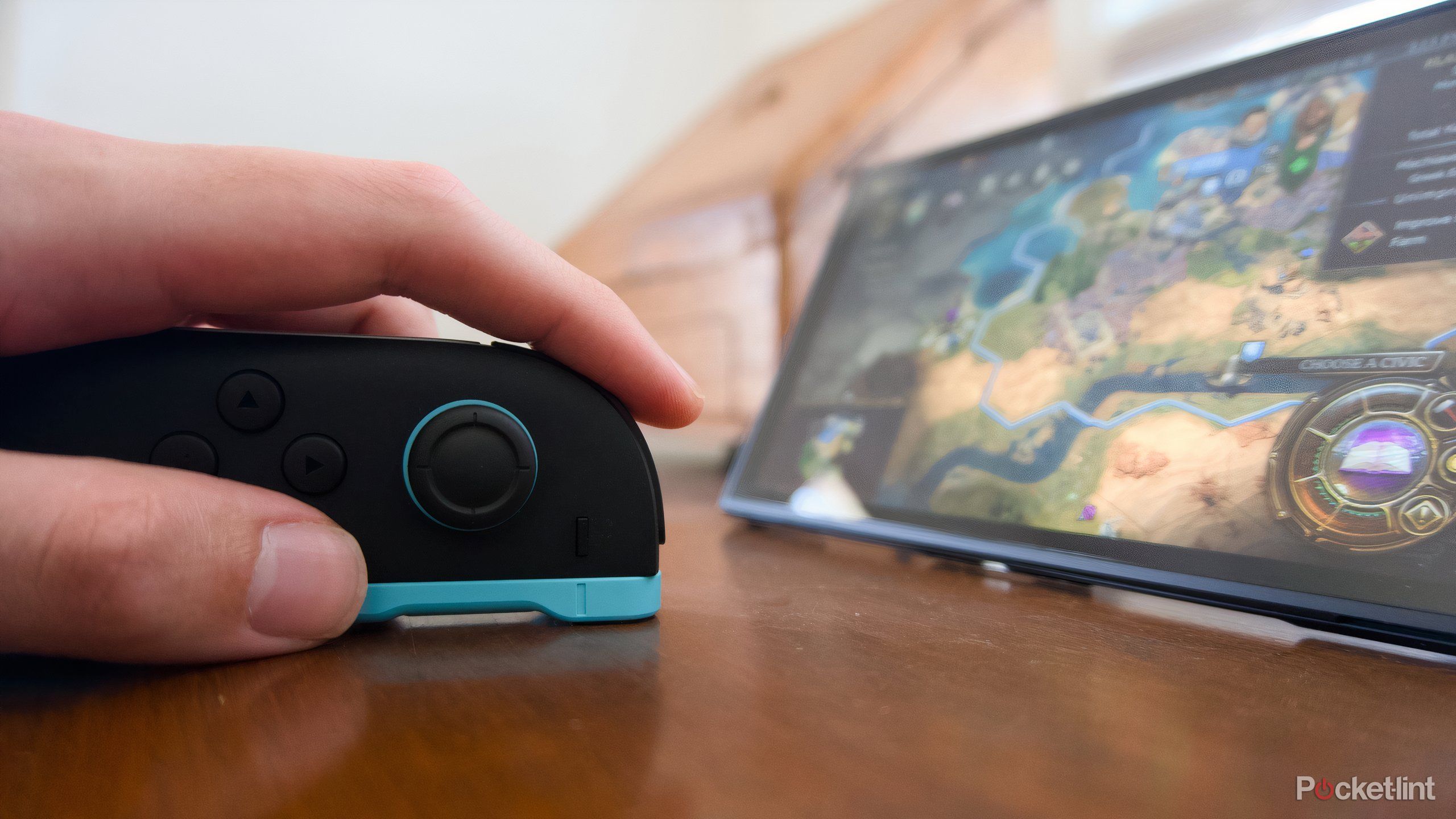 A hand dragging a blue Joy-Con 2 like a mouse in front of a Switch 2 playing Civ VII