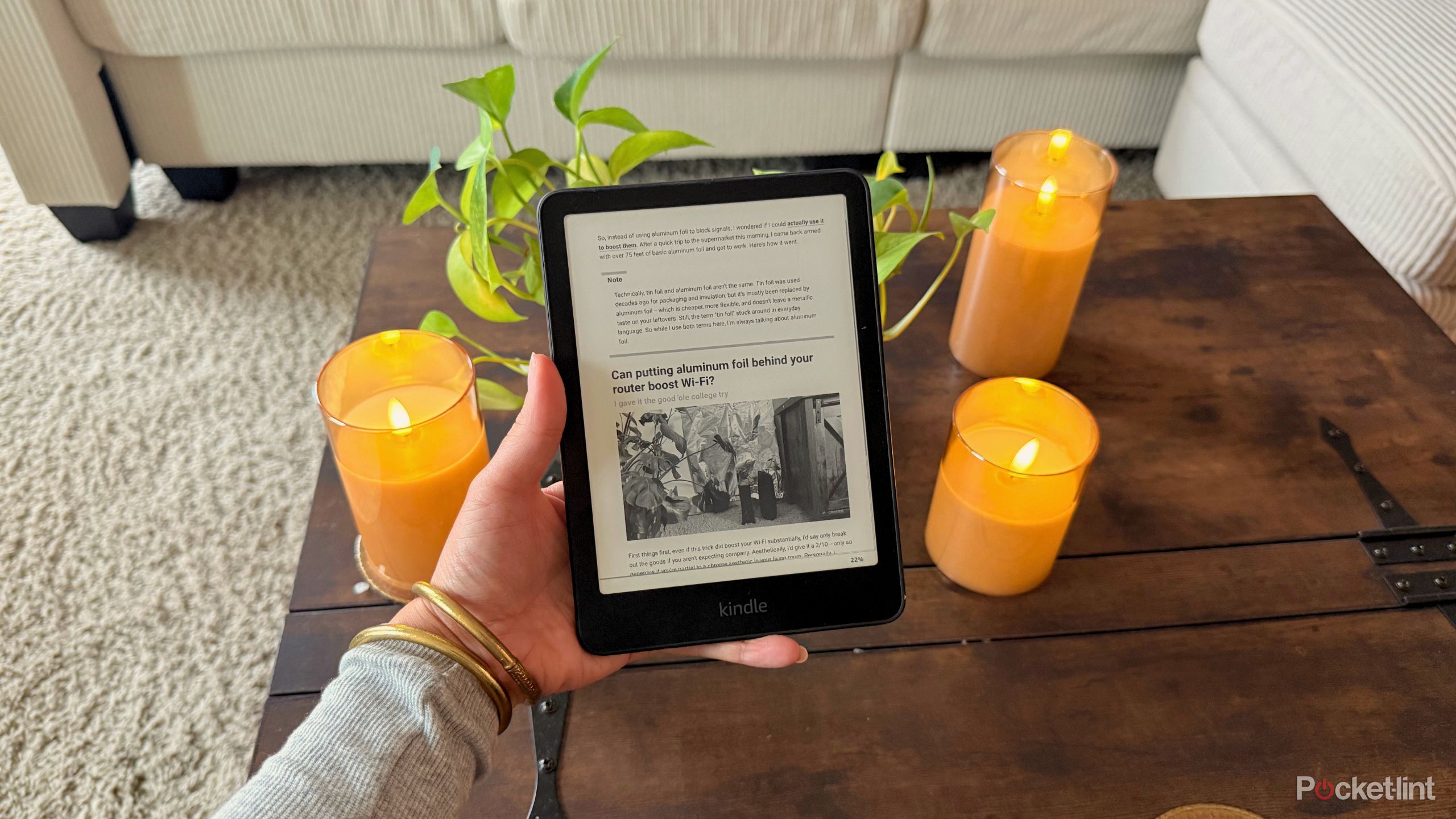 Holding a Kindle open with an article on it in front of a plant and candles. 