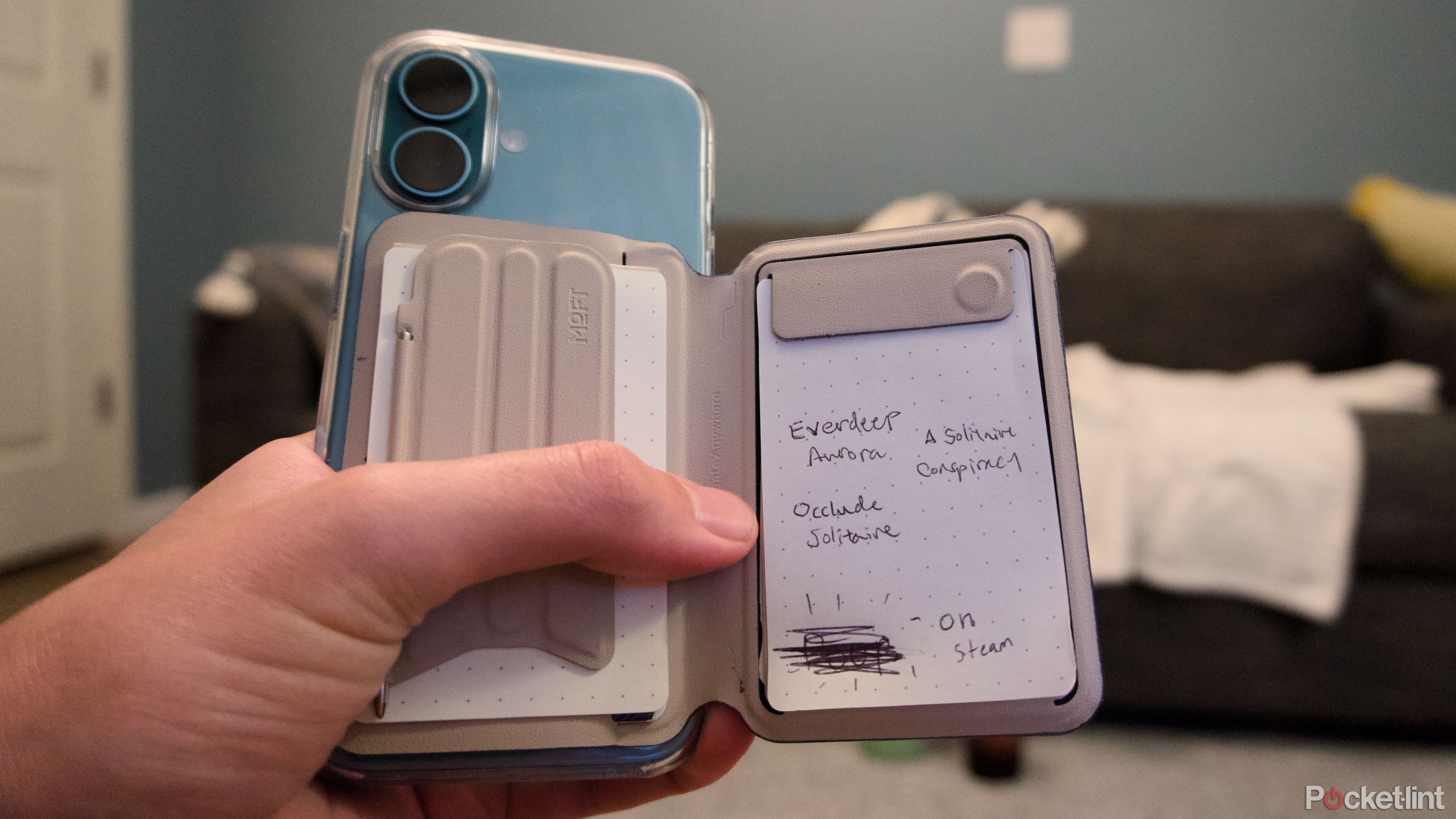 A hand holding na iPhone 16 with a magnetic notepad attached to the back.