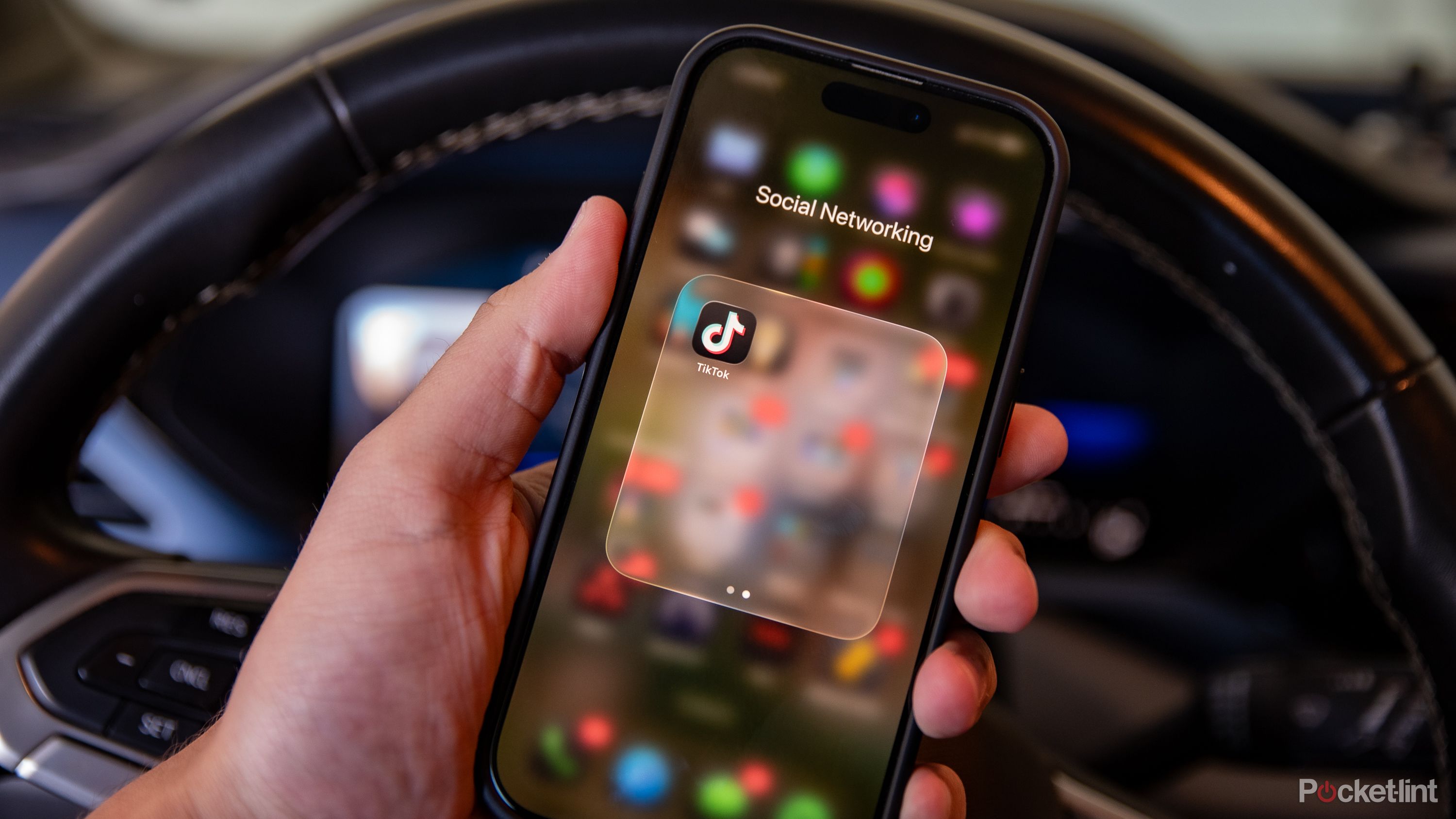 A still photo of a driver holding their phone with the TikTok app displayed. 