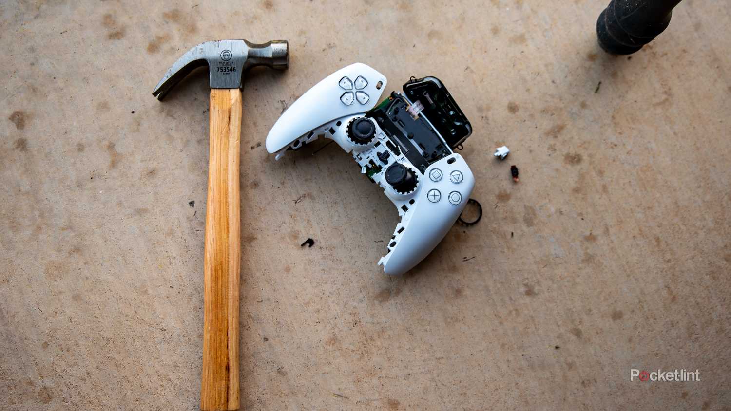 A still photo of a smashed Playstation 5 controller next to a hammer. 