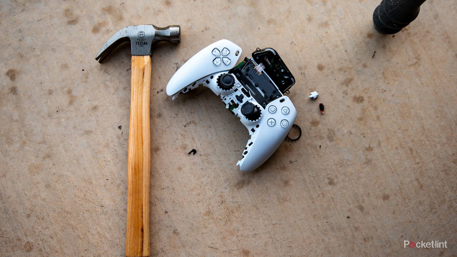 A still photo of a smashed Playstation 5 controller next to a hammer. 