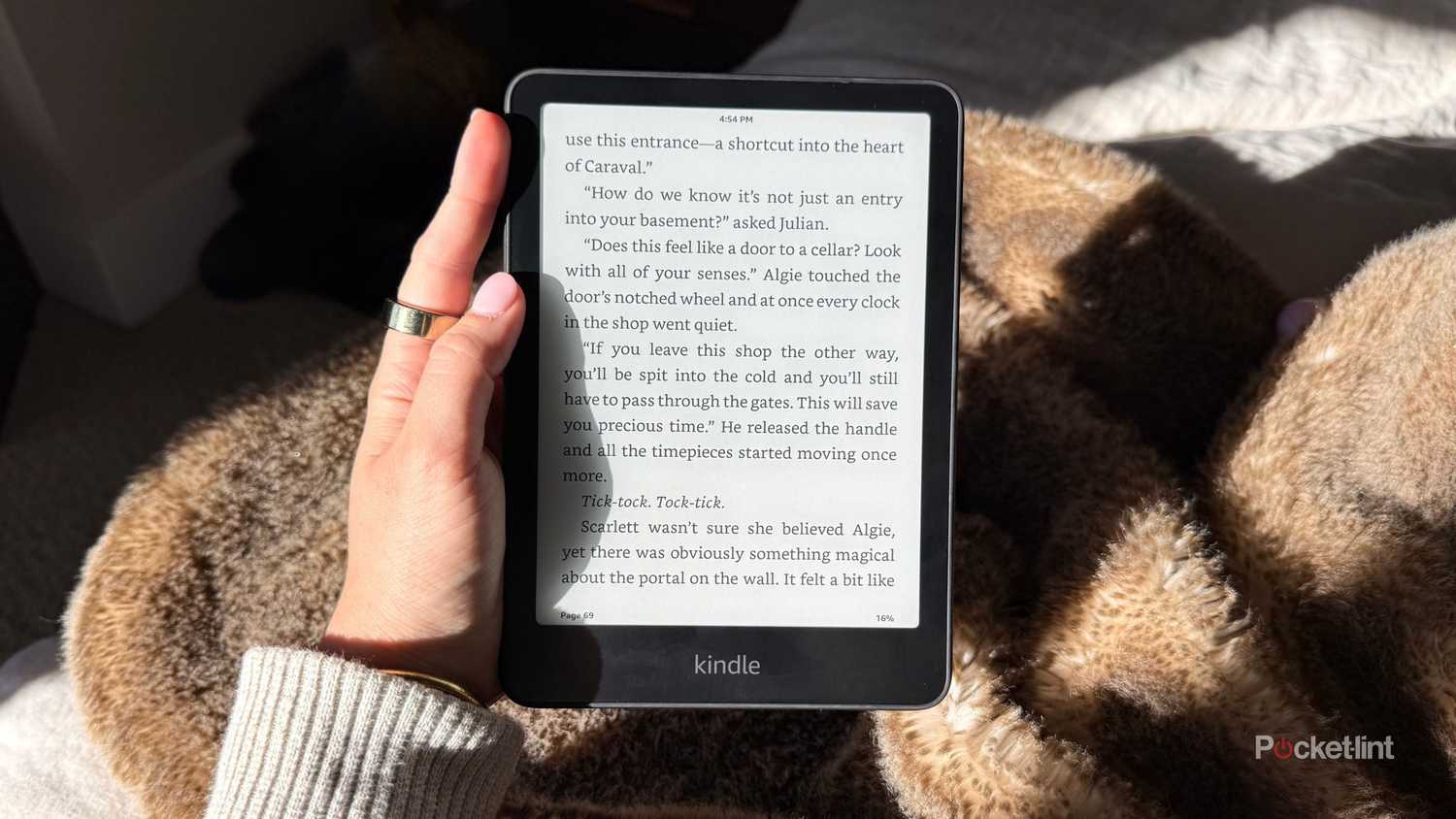 A woman holding a Kindle Paperwhite with pink nails. 