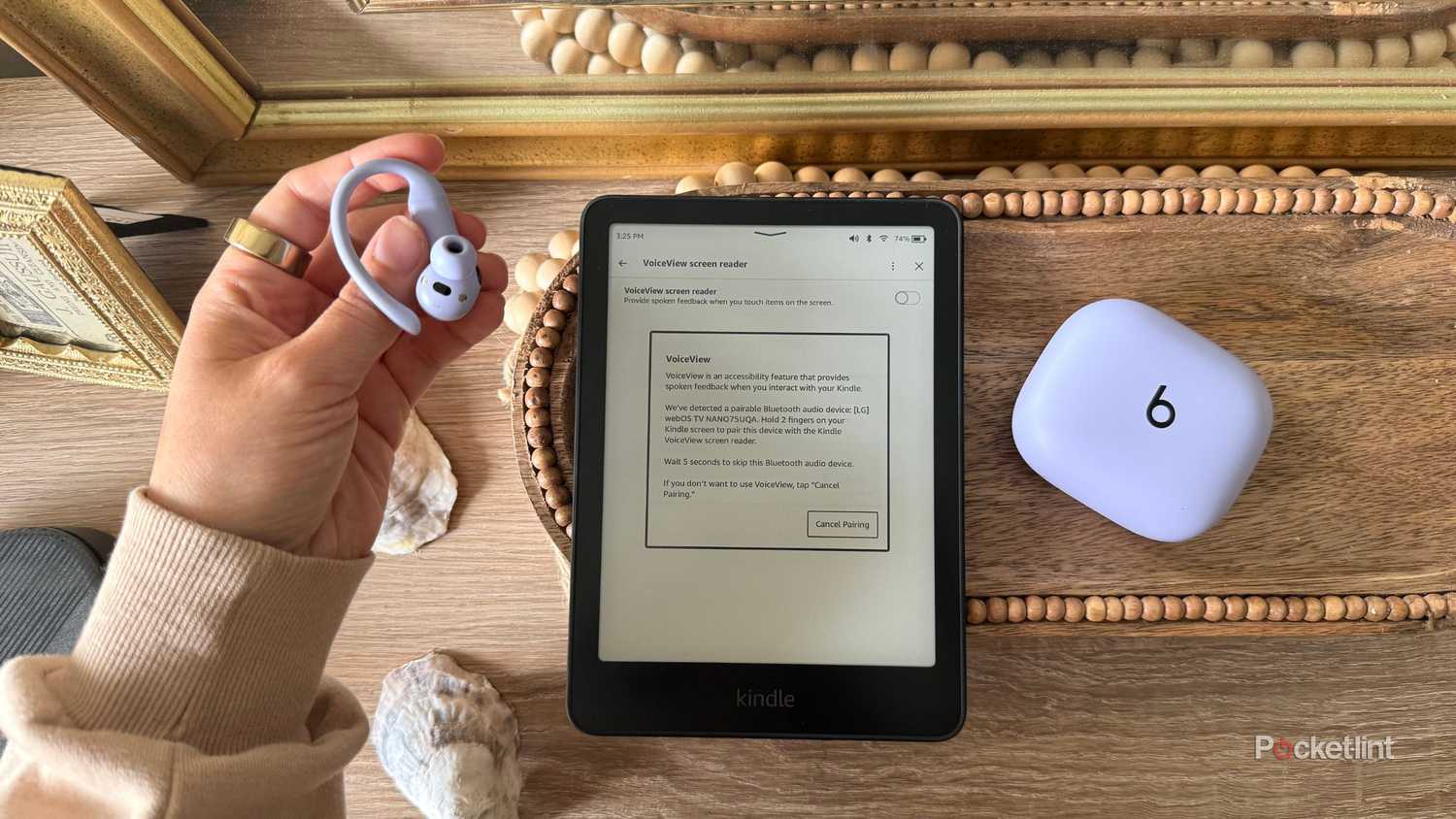 Someone holding Powerbeats beside a Kindle Paperwhite. 